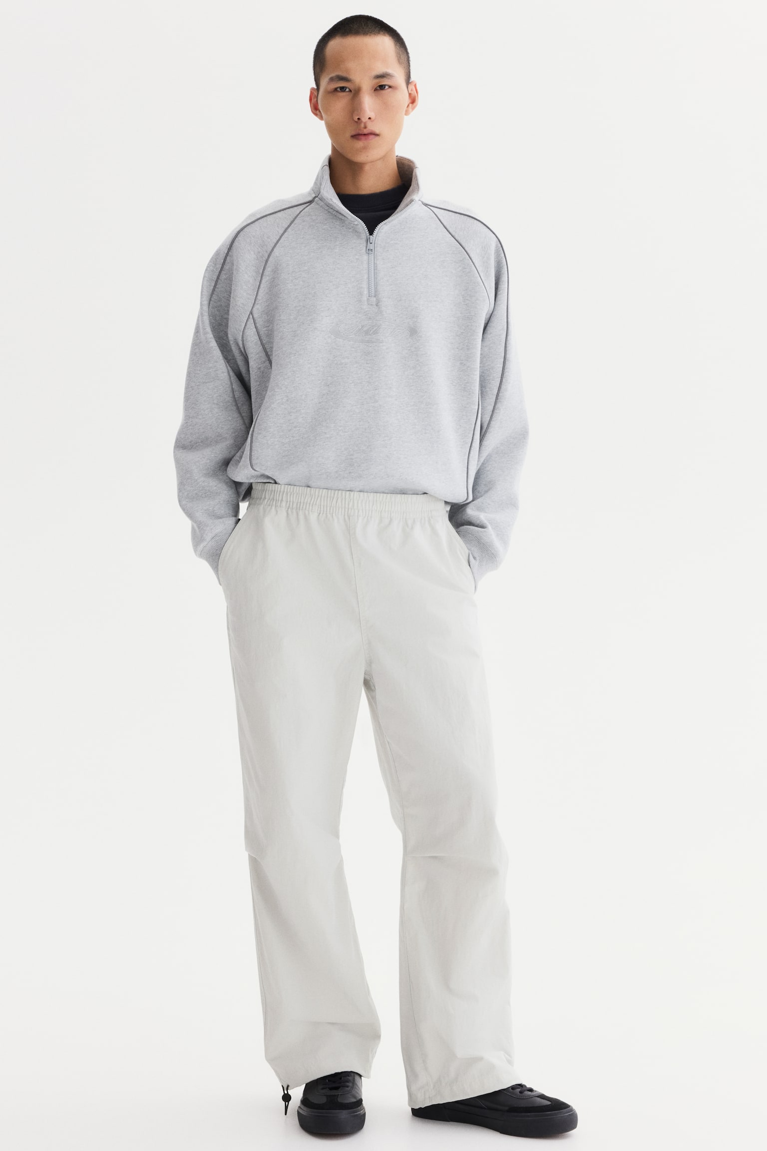 Light beige wide-leg pants feature an elasticated waistband, side pockets and adjustable drawstring toggles at the ankles. They have a relaxed fit and a lightweight, subtly crinkled texture. - 1