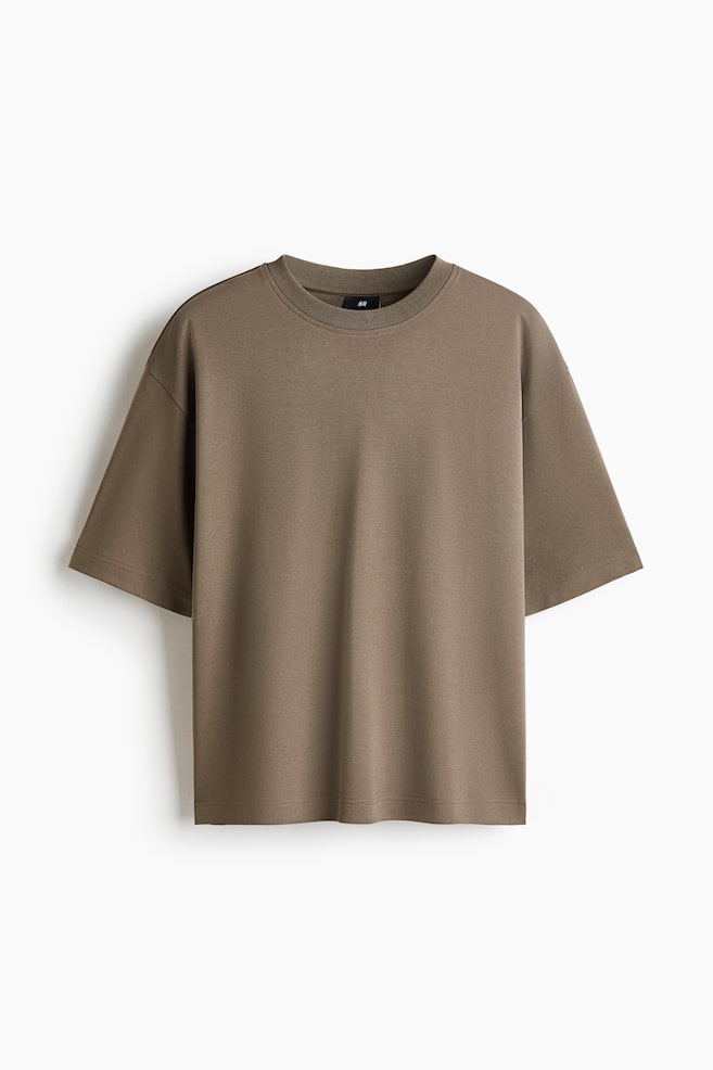 Una camiseta marrón caqui presenta un corte holgado, mangas cortas y anchas con hombros caídos, un cuello redondo acanalado y un dobladillo recto, vista desde el frente. - 1