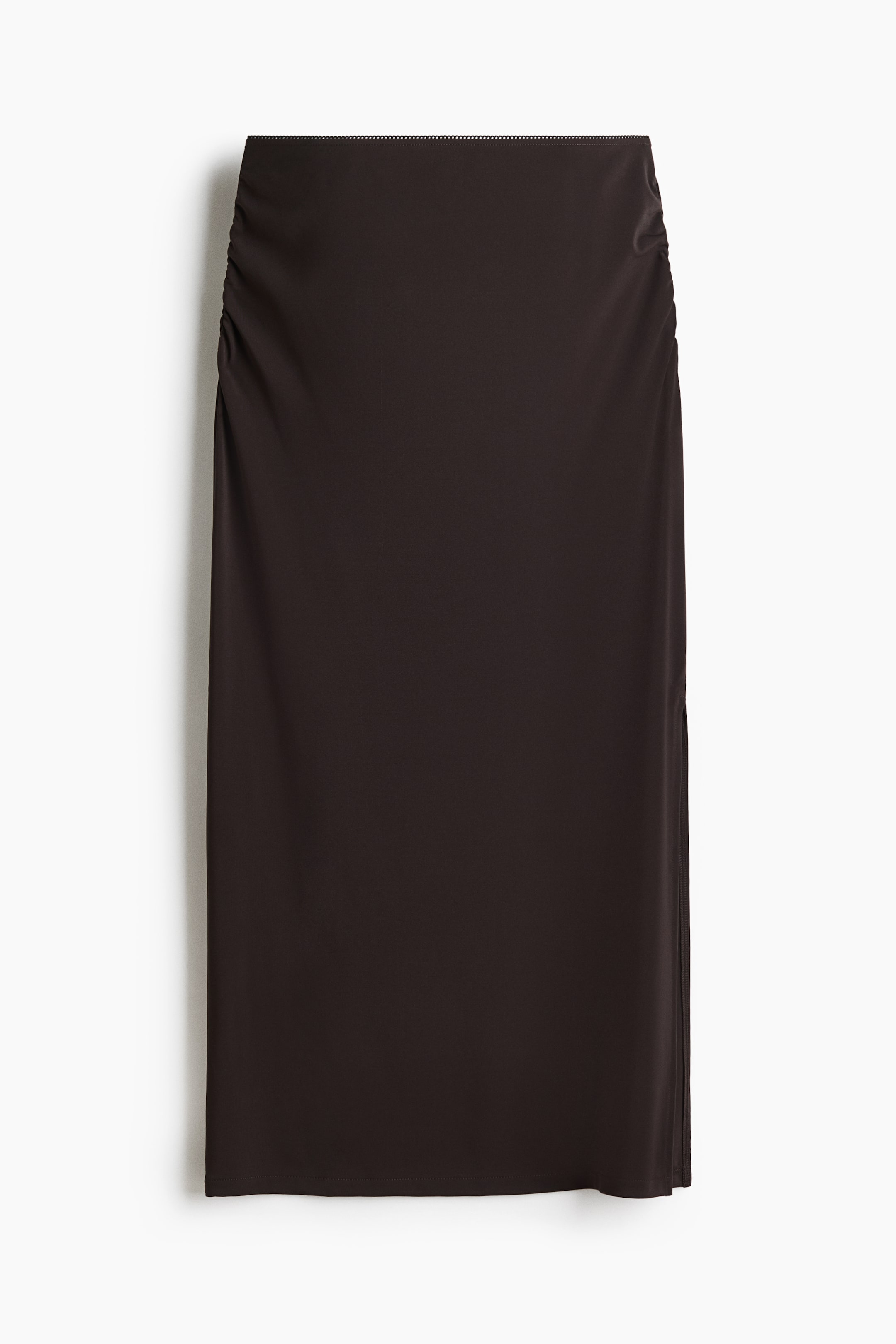 View larger image: A dark brown fitted jersey midi skirt is shown from the front, featuring a high, elasticated waist with gathers at the sides for a gently draped effect. It has a straight-cut hem with a high slit on one side.