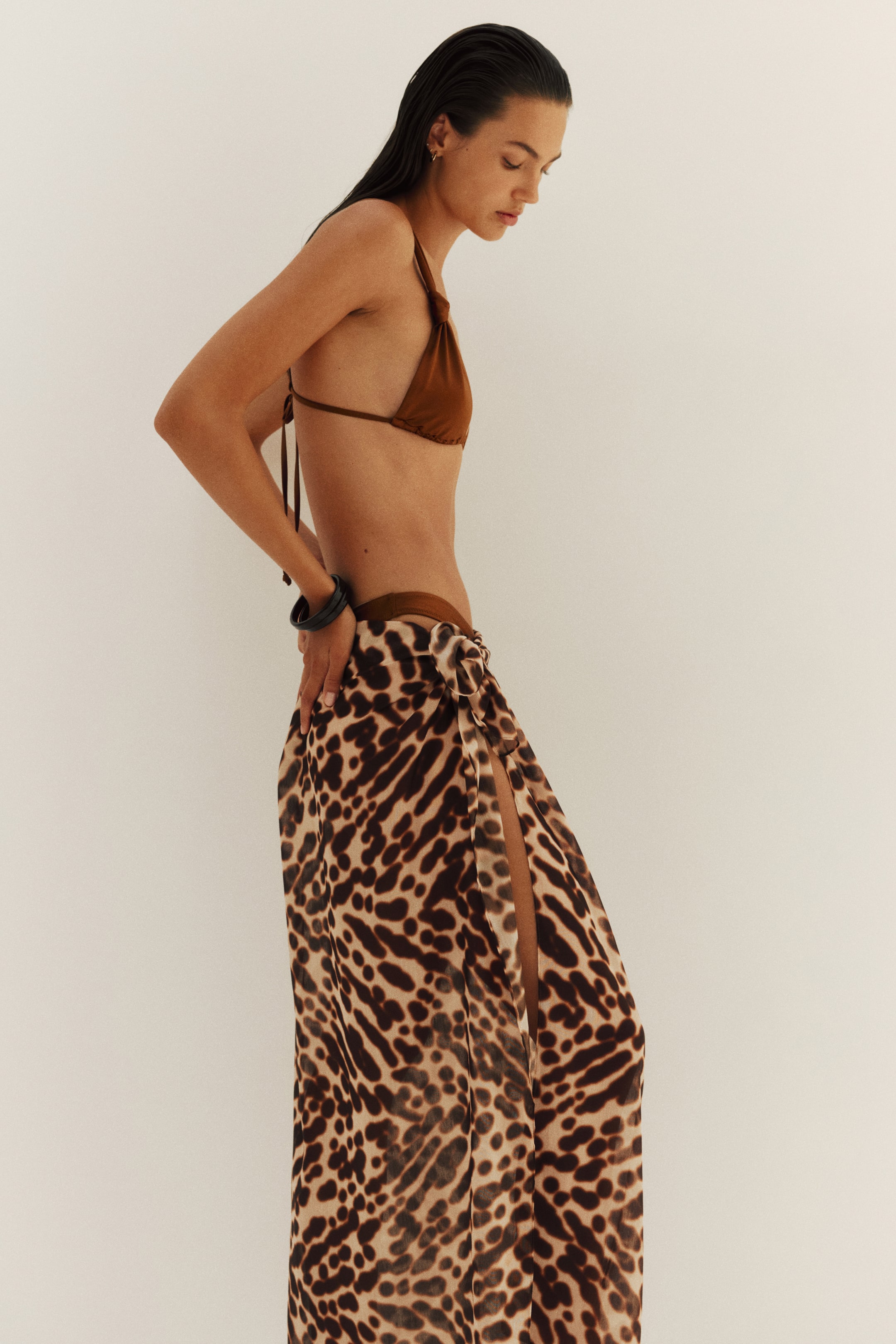 View larger image: The model is wearing a long sarong in lightweight voile featuring a brown leopard print as a skirt. It's tied at the front, creating a high slit, and covers a brown bikini bottom.