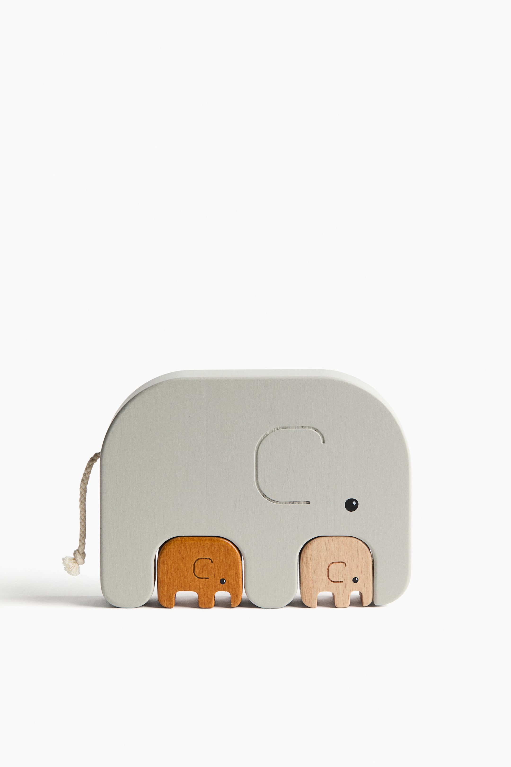 View larger image: A nesting puzzle featuring three elephant-shaped wooden toys is shown from the front, with a large light gray elephant enclosing two smaller natural wood elephants within its cutout forms. All three elephants feature carved trunk lines, while the two smaller elephants also show carved eyes and the largest elephant has a black dot eye and a braided rope tail.