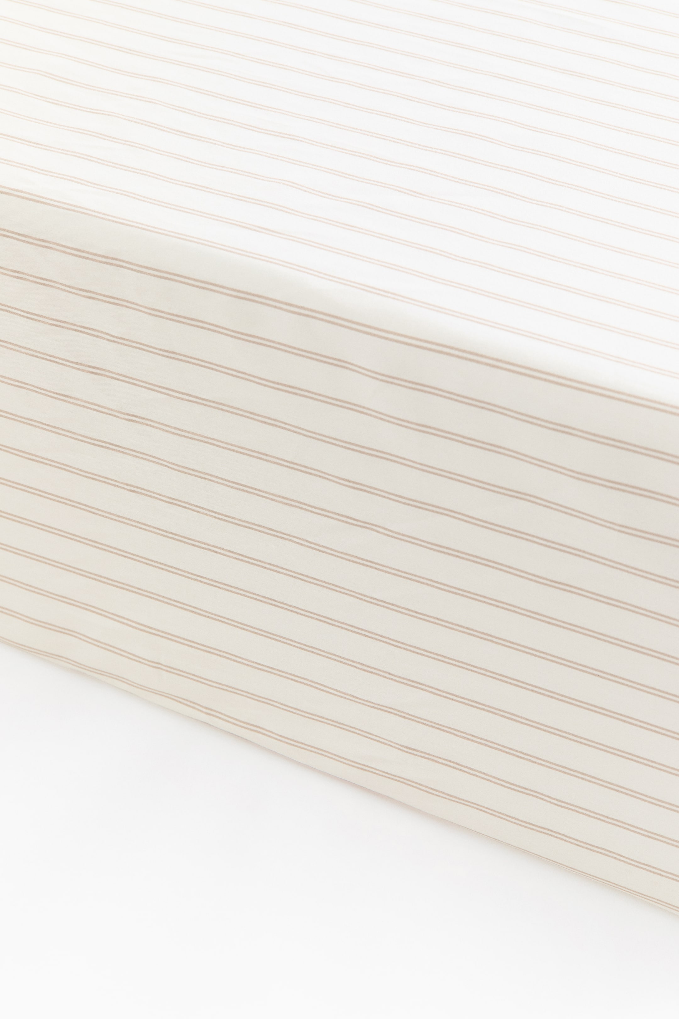 Agrandir l'image: Un drap-housse à motif en satin de coton beige clair recouvre le coin d’un matelas, présentant une surface lisse avec un motif de fines rayures brunes horizontales.