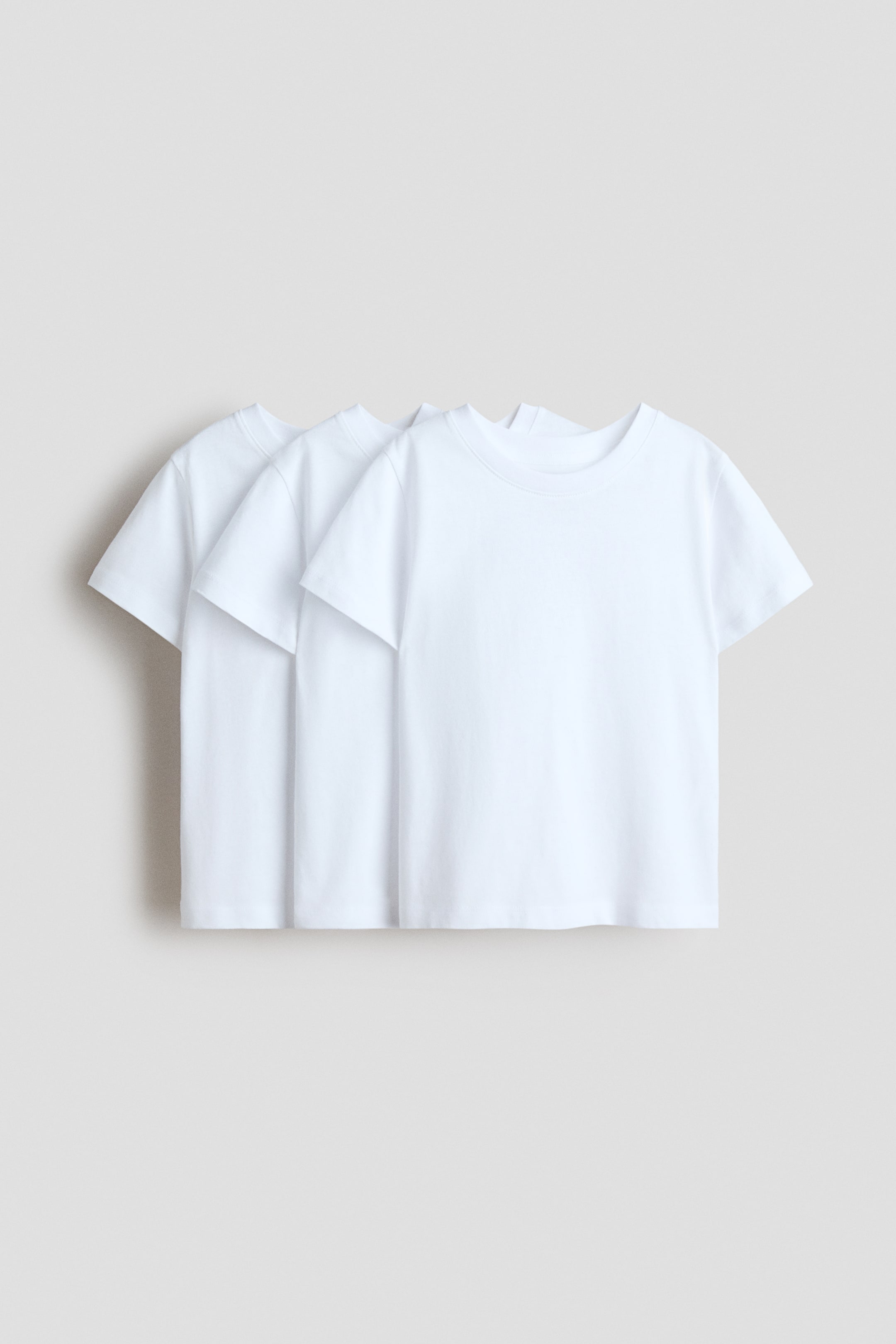 View larger image: Three white t-shirts are being presented from the front, layered one behind the other. Each t-shirt is showing a round, rib-trimmed neckline and short sleeves.