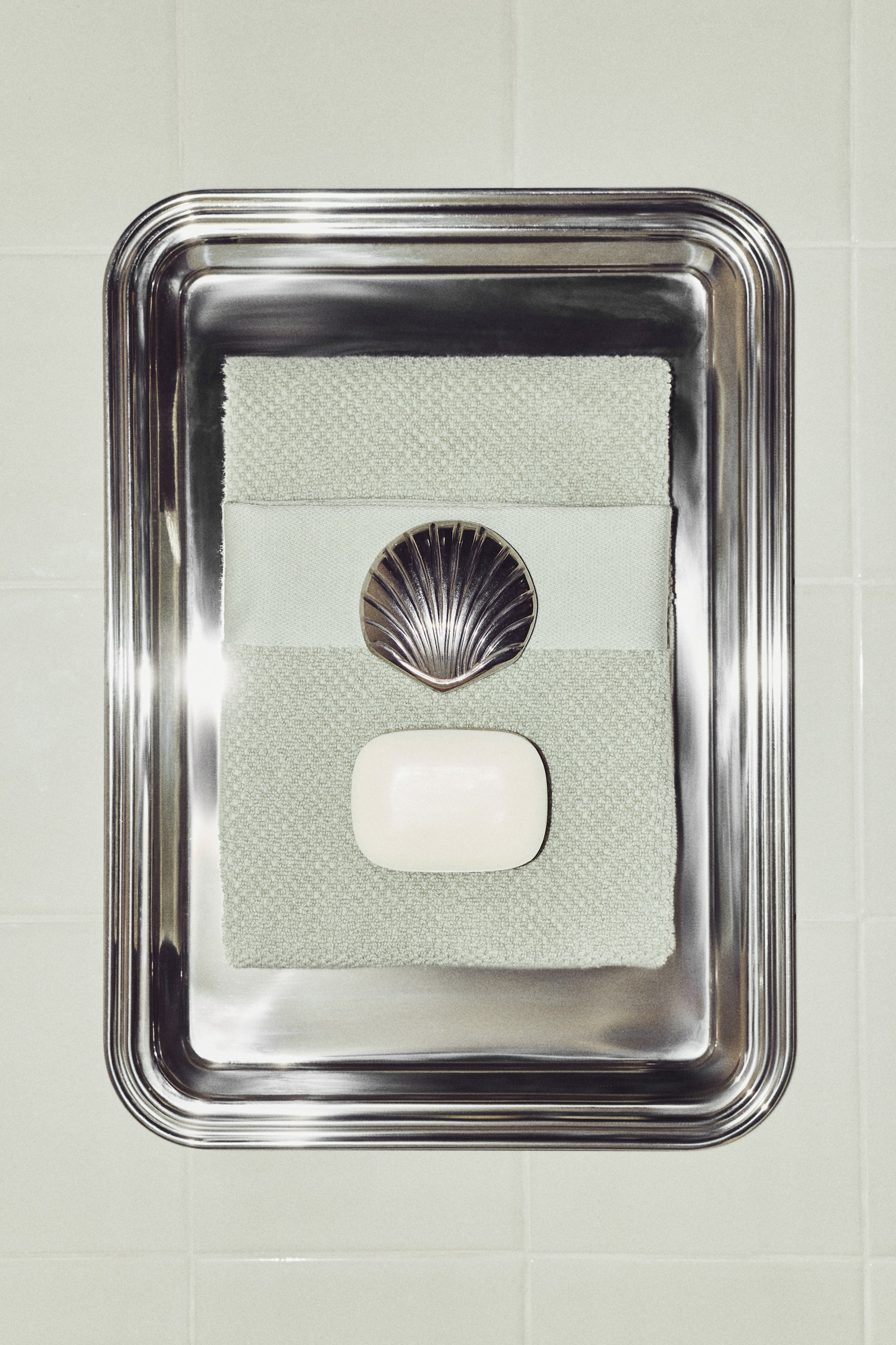 Agrandir l'image: Une serviette de toilette vert clair est posée à plat, soigneusement pliée, présentant une texture en éponge et une bande horizontale tissée plus claire et lisse au centre.