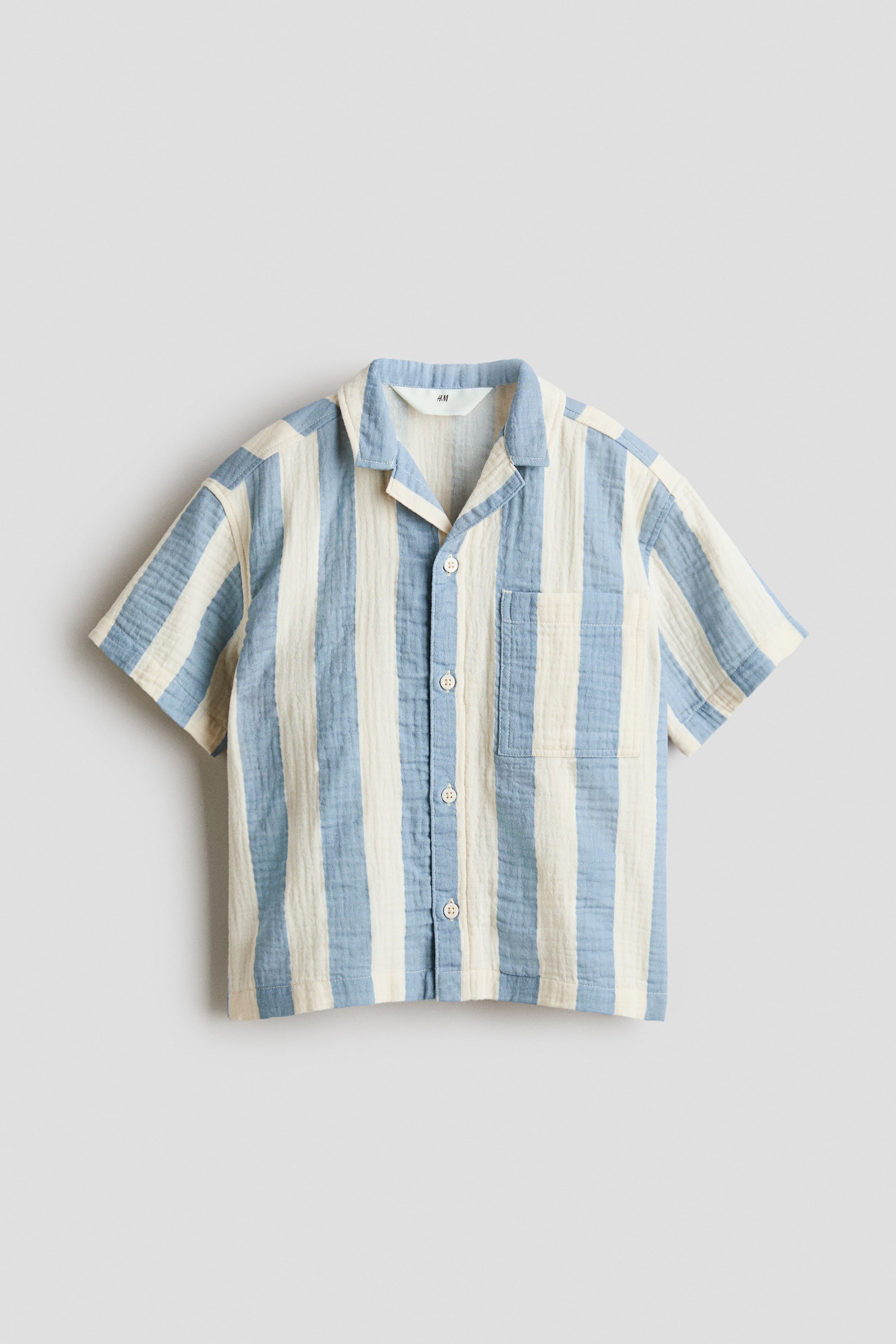View larger image: A short-sleeved shirt is presenting FRONT, showcasing vertical stripes in light blue and off-white on a textured, crinkled fabric. It is crafted with a camp collar, a full button-front closure with light-coloured buttons, and a single patch pocket on the left chest.