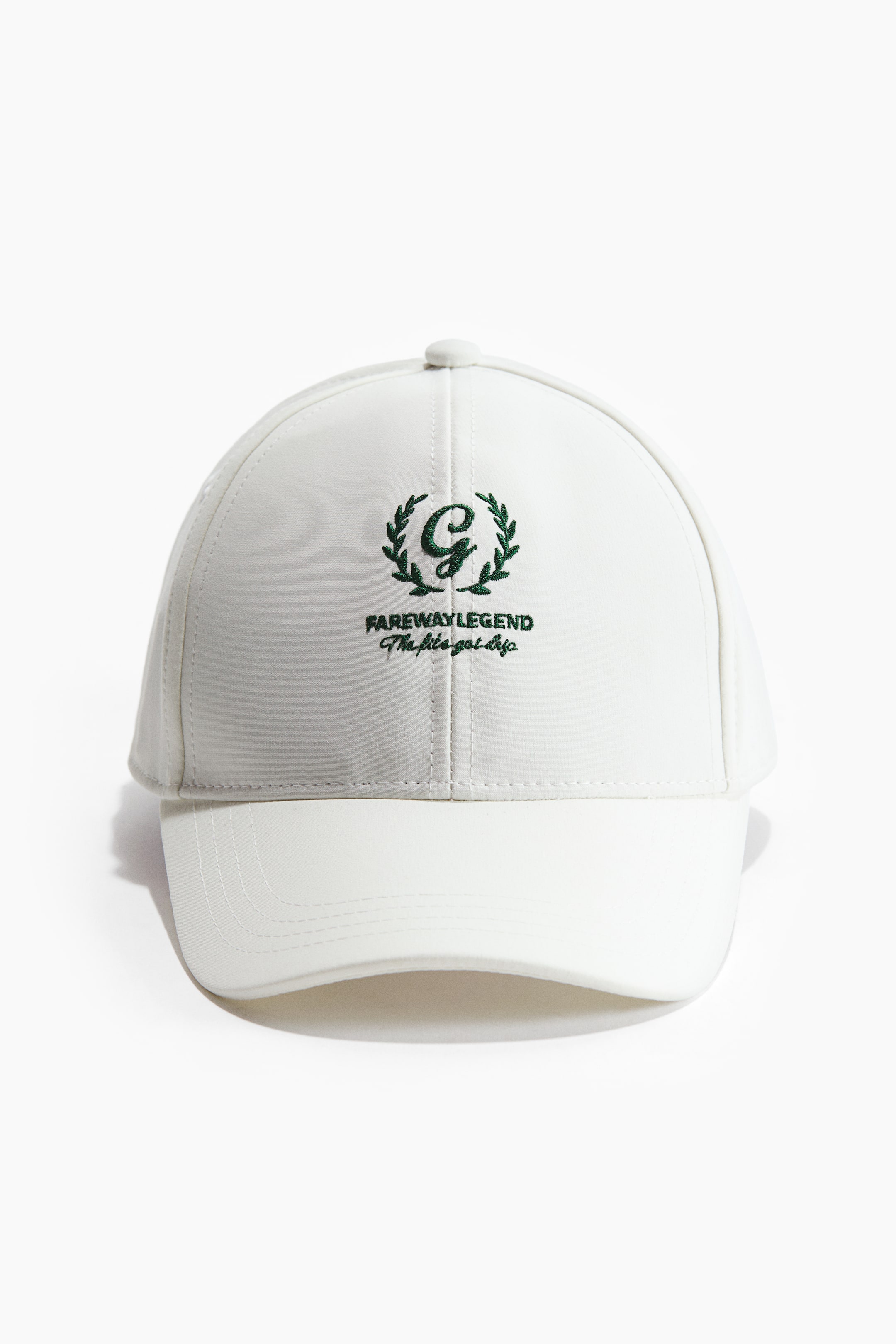 Größeres Bild anzeigen: Ein weißes Sportcap ist nach vorne gerichtet und besteht aus einem glatten, strukturierten Stoff. Auf der Vorderseite ist ein grünes, gesticktes Logo zu sehen, das ein großes 'G' in einem Kranz, die Worte 'FAREWAY LEGEND' und 'The life got drip' in einer Schreibschrift umfasst.