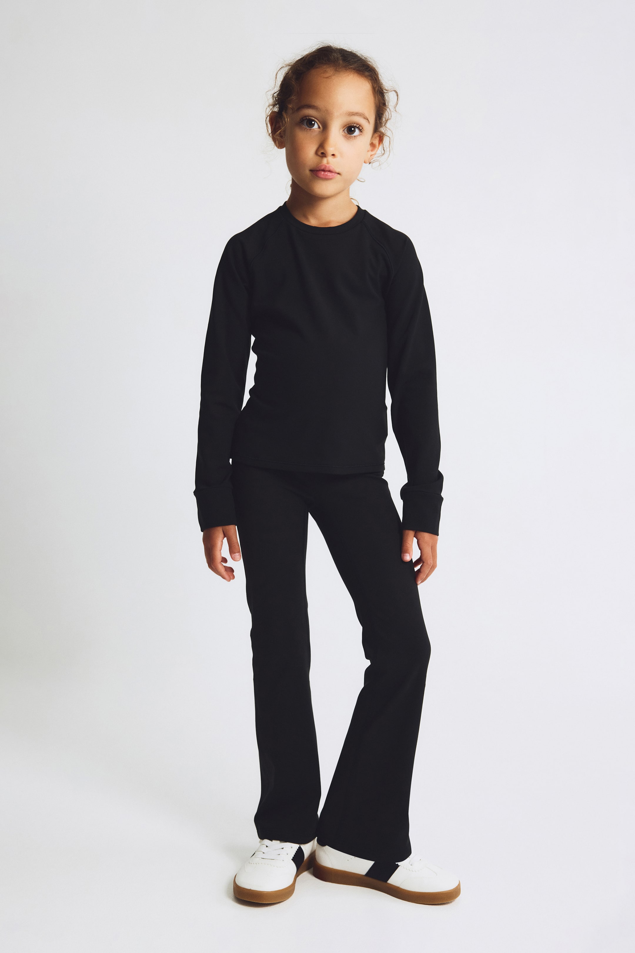 Agrandir l'image: Un ensemble noir assorti en deux pièces est présenté de face, comprenant un haut à col rond à manches longues avec manches raglan et poignets côtelés. Le pantalon coordonné est ajusté au niveau des cuisses puis s’évase vers les chevilles.