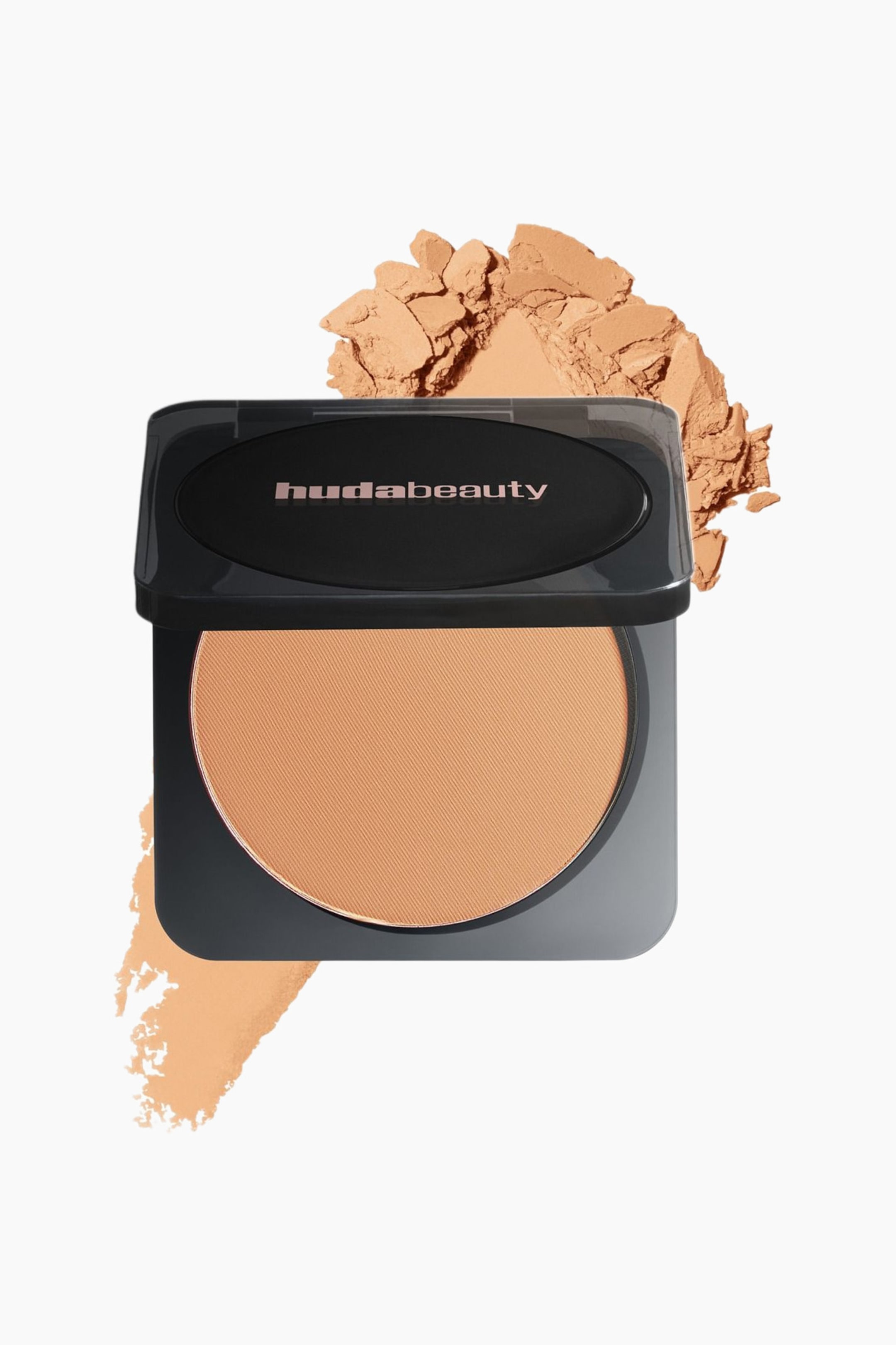 Visa större bild: En svart Huda Beauty-kompakt öppnas och visar en rund puck med mellanbrunt pressat puder som har en subtil diagonal textur. Lösa klumpar av samma puder samlas bakom kompaktet, och en puderswatch sträcker sig nedanför det.