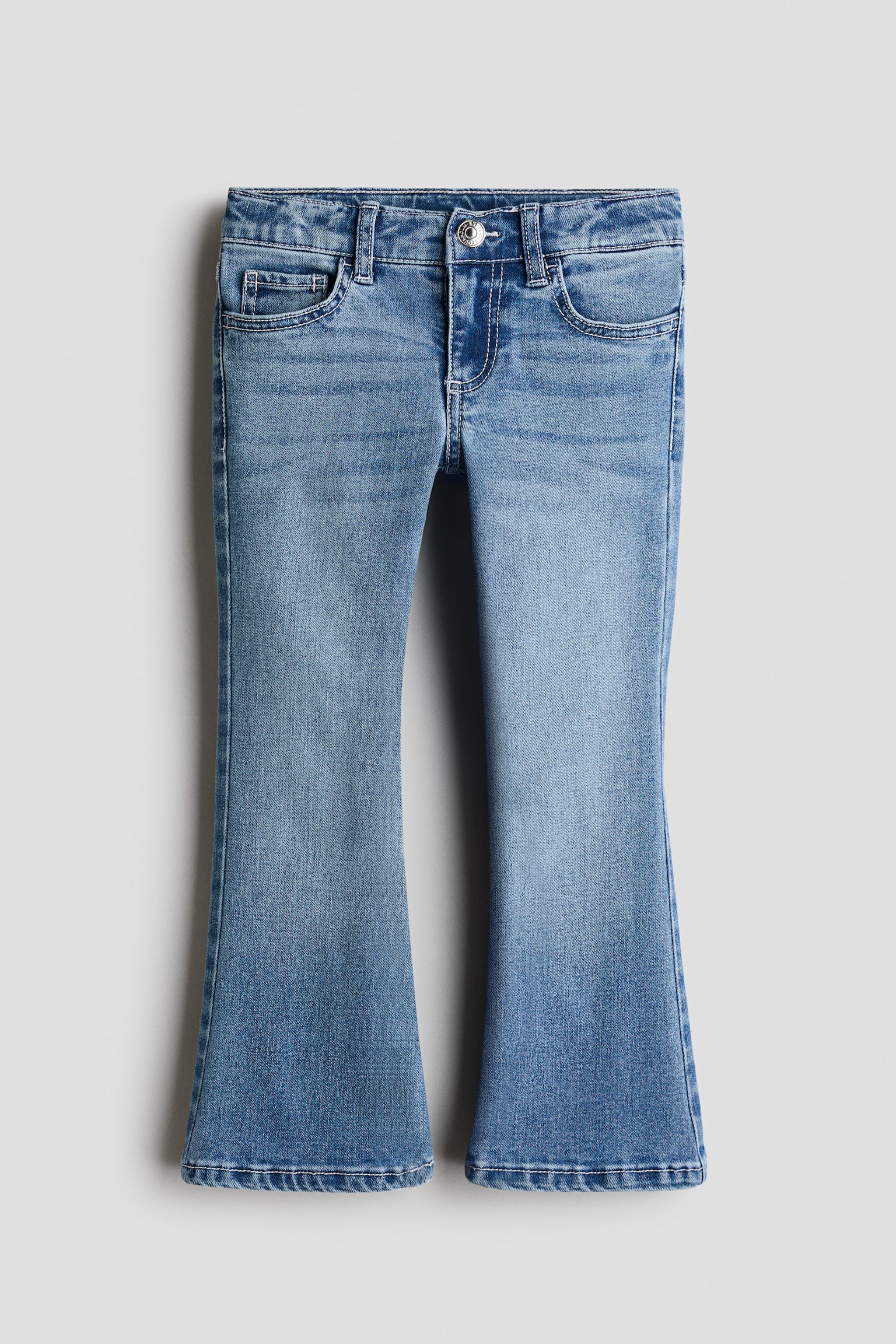 A pair of blue wash flared jeans is shown from the front, featuring a classic five-pocket design with a metal button fastening and belt loops at the waistband. The jeans display subtle fading along the thighs and widen into a flare from the knee to the hem.