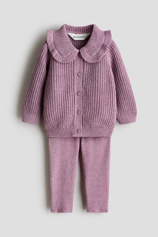 A lilac two-piece knitted set is presented flat lay, front-facing. The cardigan is featuring a ruffled round collar, long sleeves, a ribbed hem, and a front button closure. The coordinating pants are displaying a matching vertical ribbed knit texture. - 1