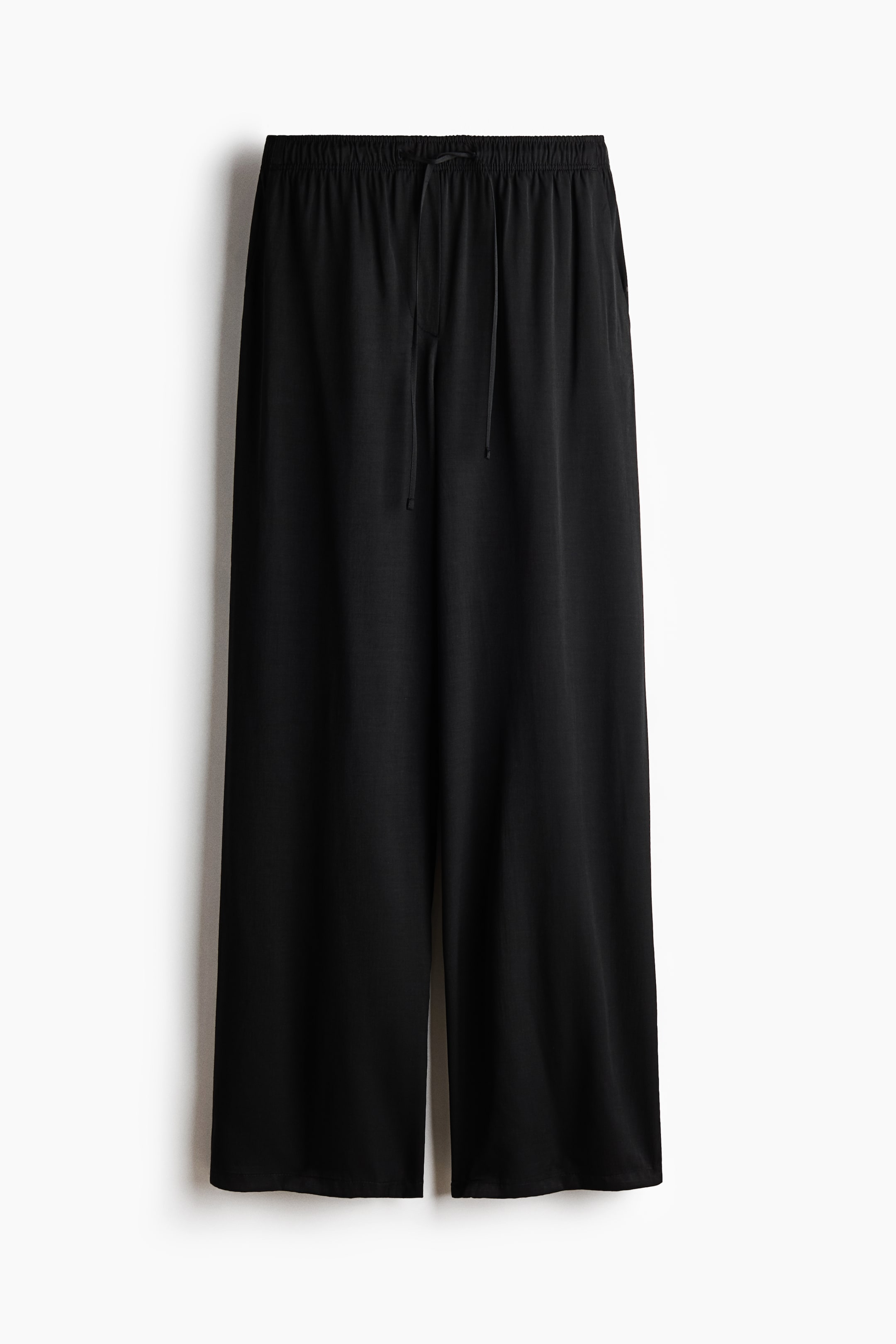 View larger image: Black wide-leg pants are shown from the front. They feature an elastic waistband with a central drawstring tie and wide, straight legs that fall to an ankle length.