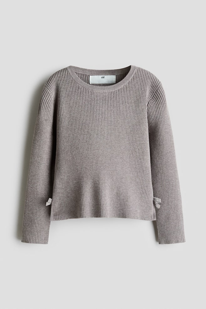 Se muestra por delante un jersey de punto canalÃ© denso en color topo apagado, con cuello redondo rematado en canalÃ©, mangas largas y bajo recto. El jersey incluye pequeÃ±as aberturas laterales en el bajo, decoradas con diminutos lazos de tejido a juego. - 1