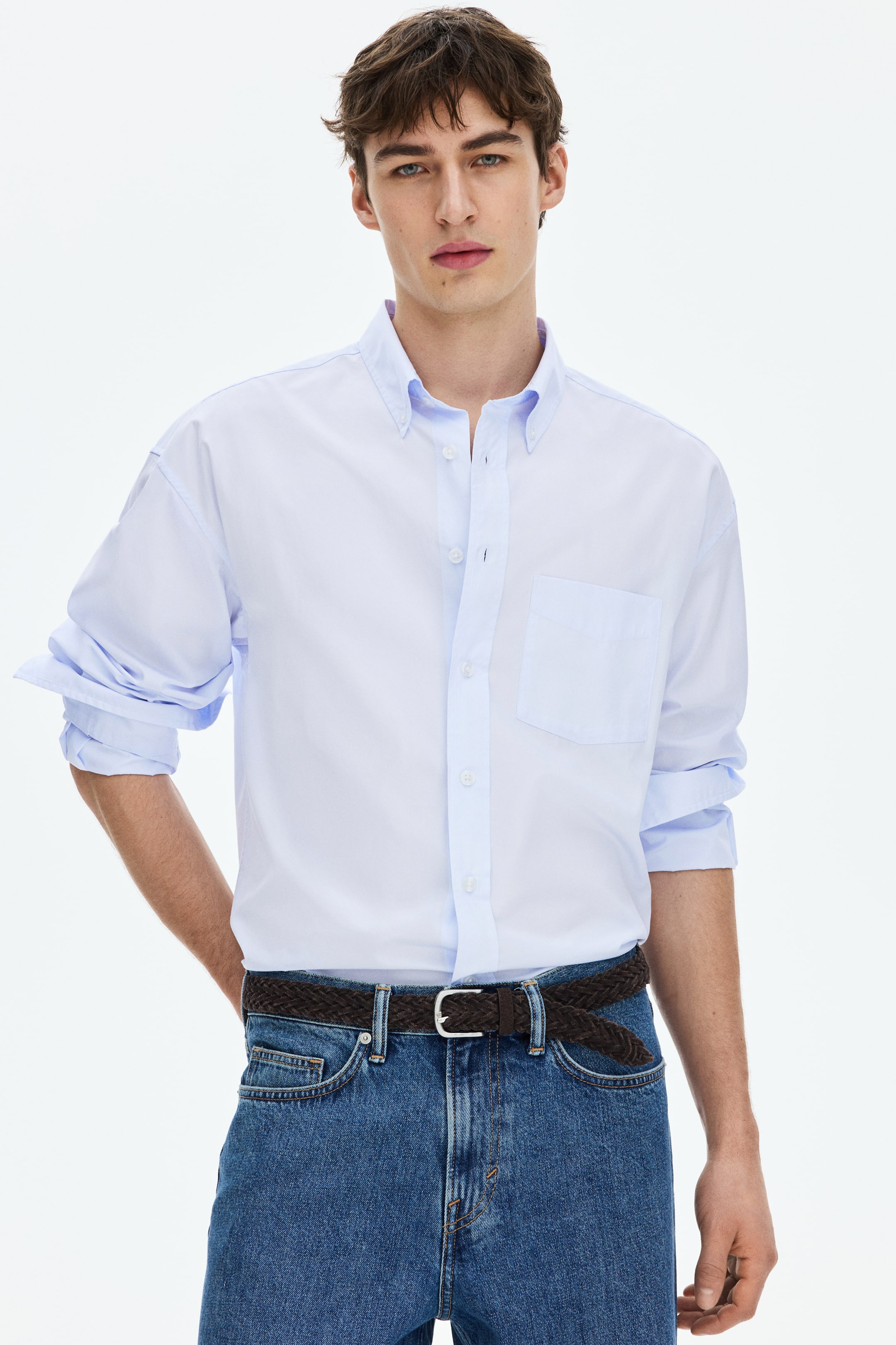 View larger image: A light blue relaxed-fit shirt, featuring a button-down collar, a classic front, and an open chest pocket, is being worn by the model. Its long sleeves are being rolled up, and the shirt is being tucked into blue jeans.