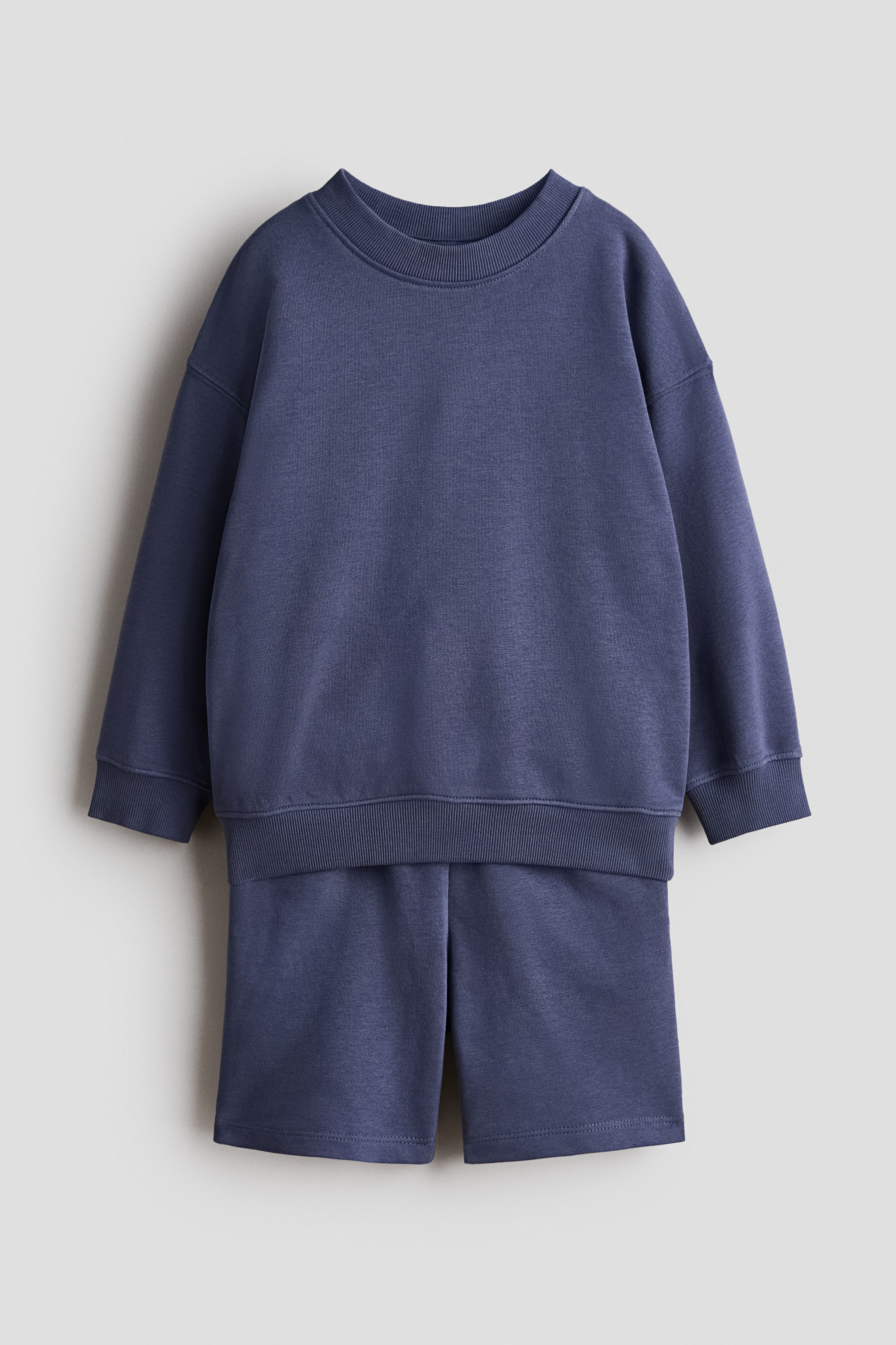 Visualizza immagine più grande: Un set frontale presenta un top a maniche lunghe e pantaloncini coordinati, entrambi realizzati in un leggero tessuto felpato blu polvere. Il top è progettato con un girocollo a coste, spalle scese, polsini a coste e un orlo a coste, mentre i pantaloncini presentano una vestibilità semplice e rilassata.