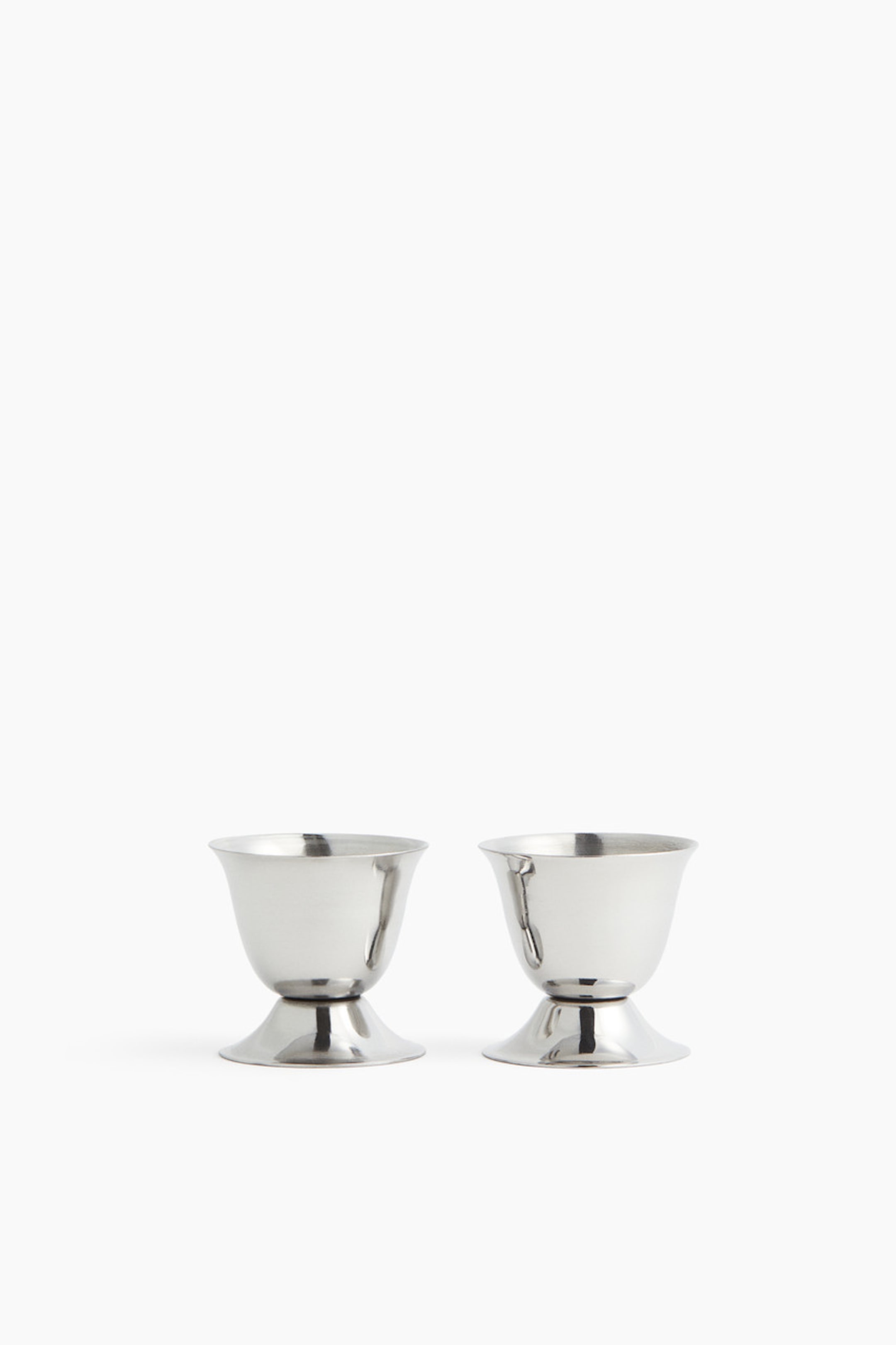 View larger image: A pair of stainless steel egg cups is presented, each featuring a rounded cup and a flared, circular base.