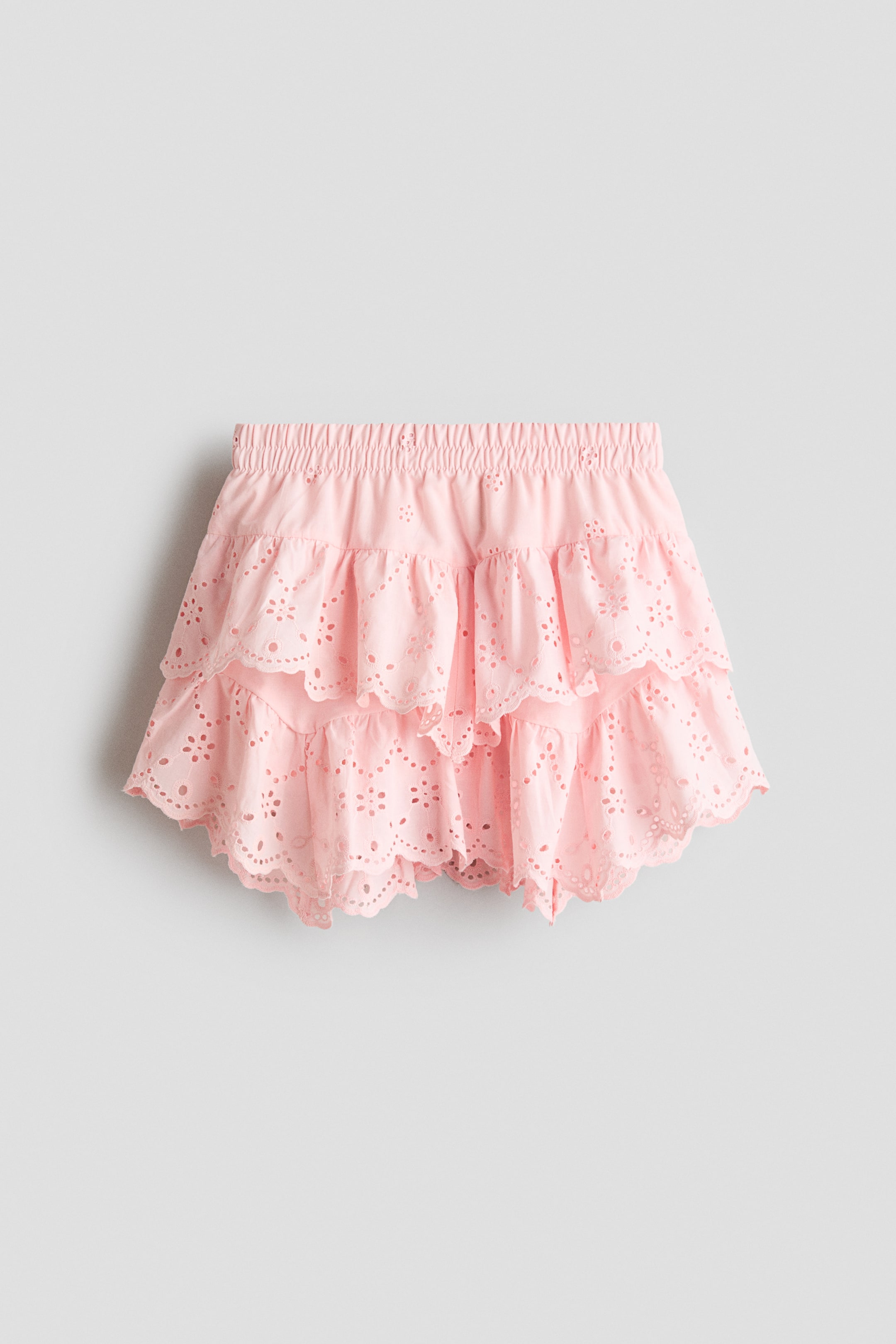 View larger image: A pink tiered skirt is facing front, featuring a covered elasticated waist and two ruffled tiers detailed with broderie anglaise.