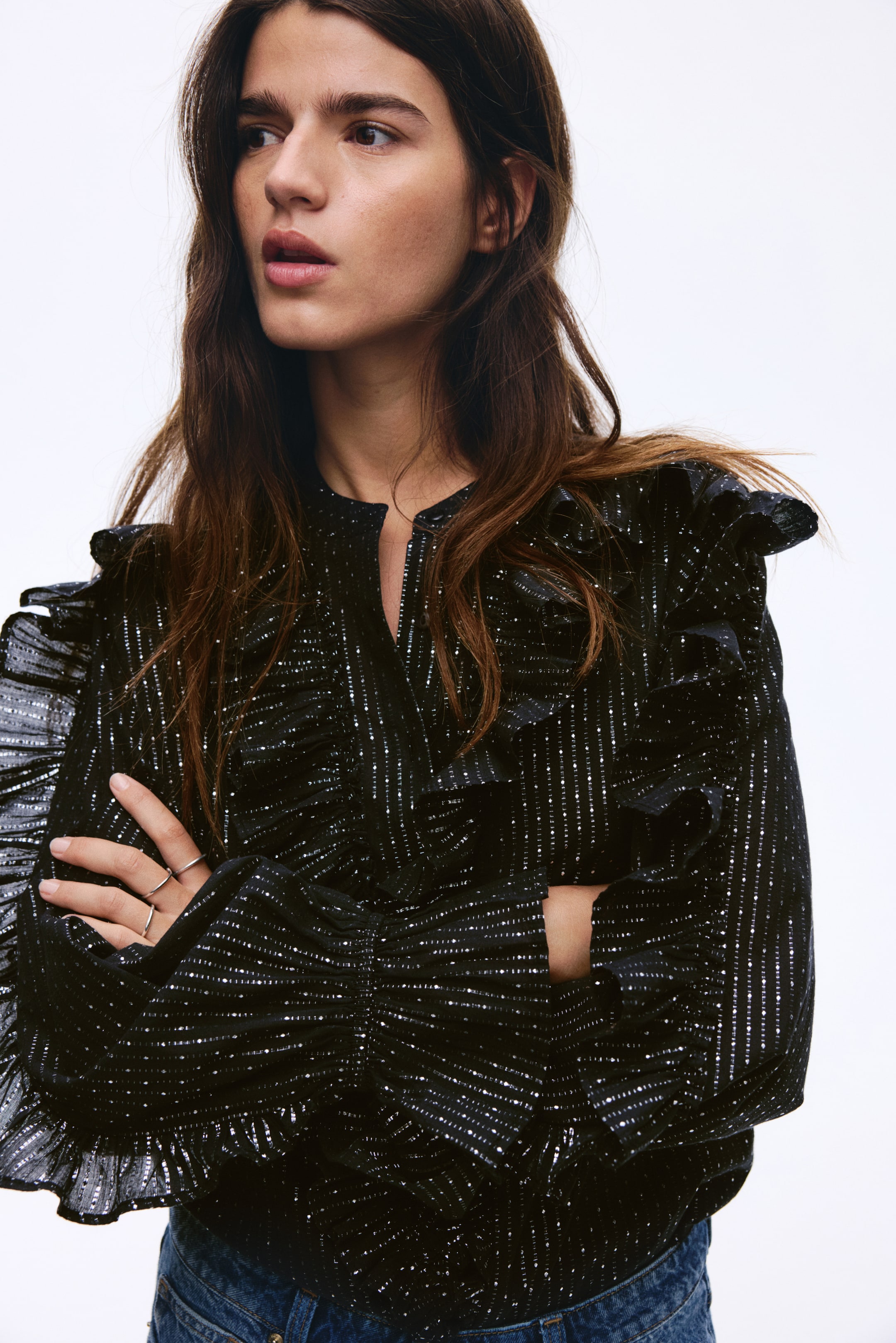 Agrandir l'image: Une blouse bleu marine est orientée légèrement sur le côté, avec des rayures verticales argentées scintillantes et des points tout au long de son tissu. Elle est conçue avec un col fendu et des volants proéminents sur les épaules, qui descendent le long des manches longues rassemblées avec des fronces aux poignets.