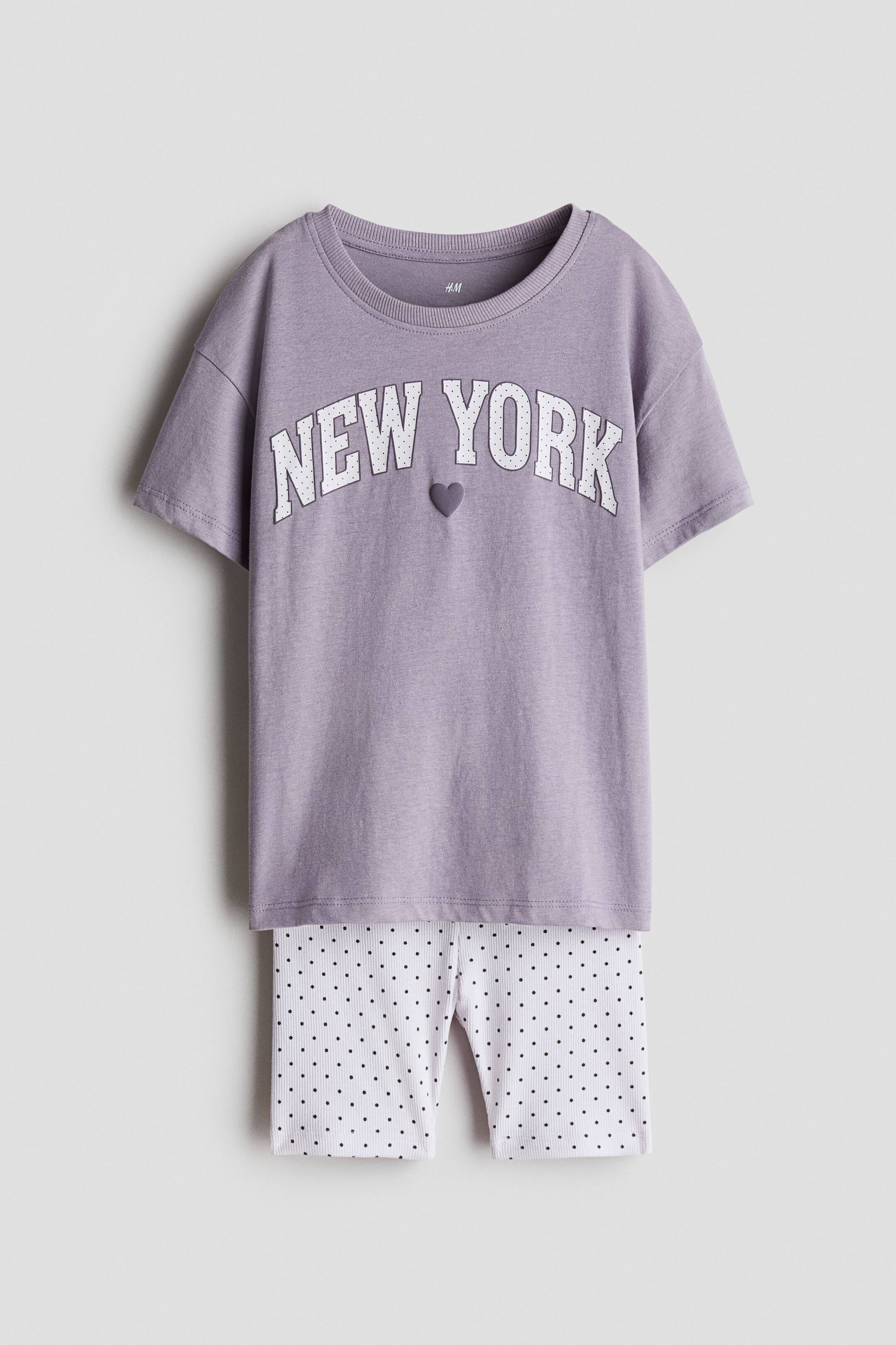 View larger image: A two-piece lounge set is shown from the front, featuring a light purple short-sleeve T-shirt and white ribbed shorts with a black polka-dot pattern. The T-shirt features a ribbed crew neck and arched "NEW YORK" text in white varsity lettering with a small purple heart below it.