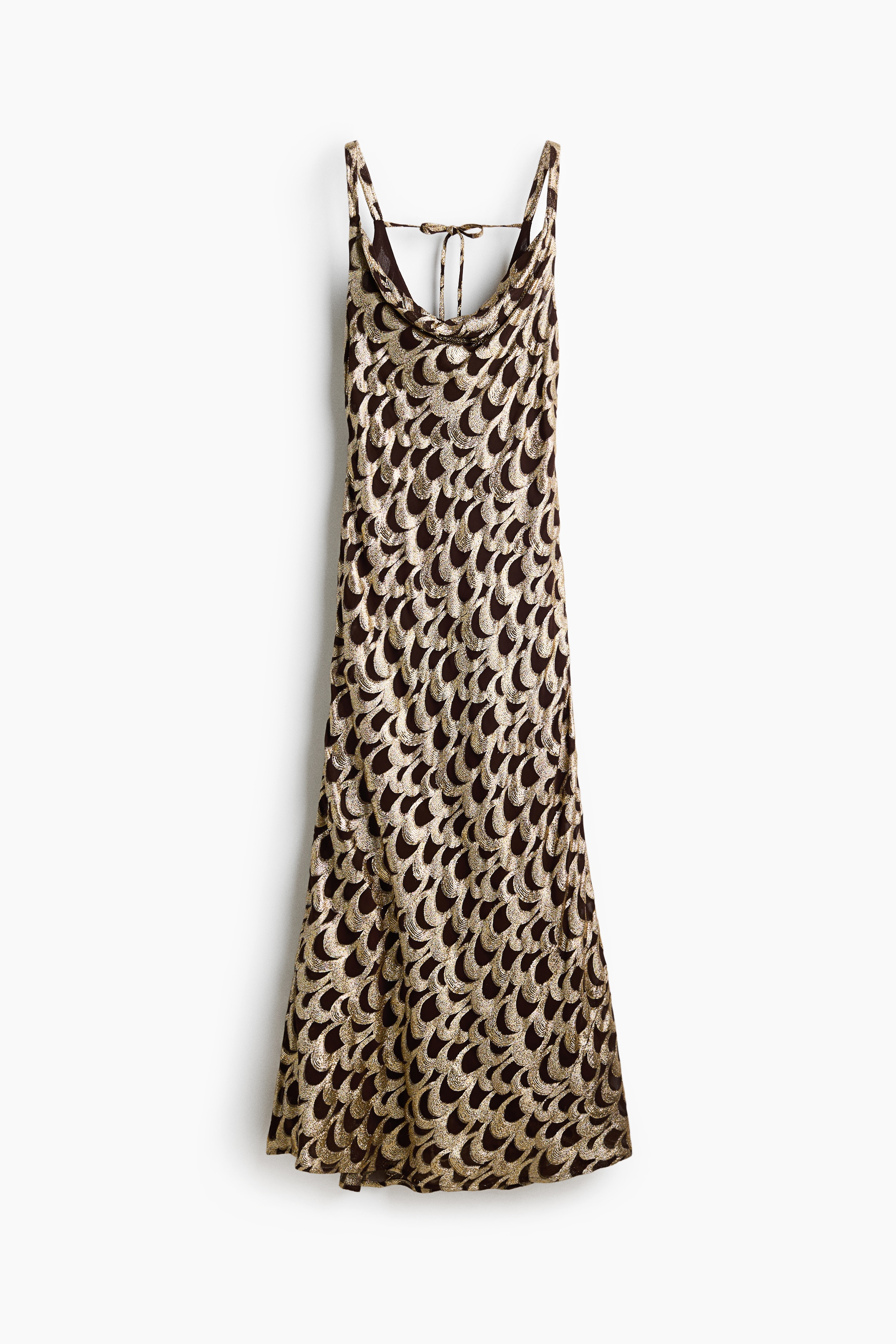 A long, sleeveless dress in a shimmering gold and dark brown jacquard-weave pattern is being worn by the model. The dress features narrow shoulder straps, a draped cowl neck, and a gently flared skirt that reaches the floor.