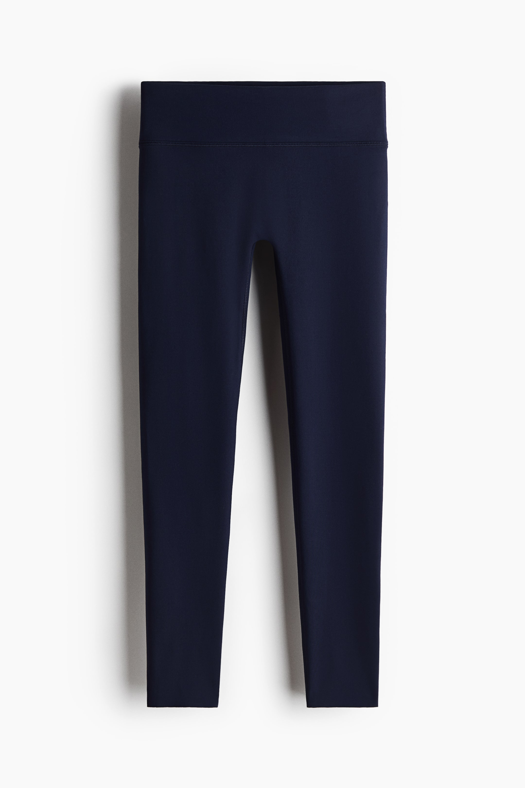 Visualizza l'immagine ingrandita: I leggings sportivi blu navy sono distesi in piano e rivolti frontalmente, con un'ampia fascia in vita a vita alta. Presentano una finitura liscia e opaca e una lunghezza cropped, che termina sopra la caviglia.