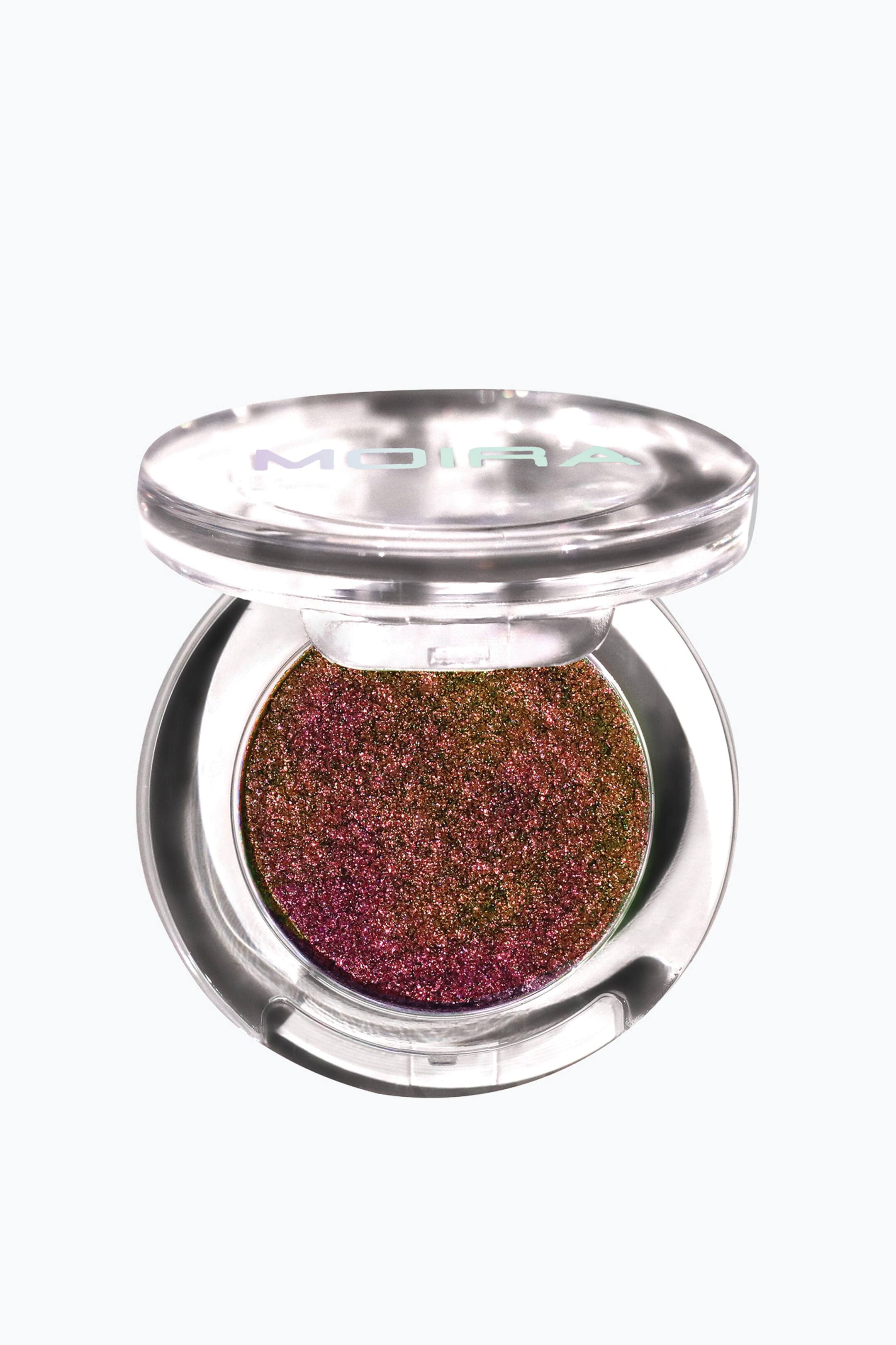 Vis større bilde: Supernova Glitz Shadow ligger i en åpen, rund, gjennomsiktig plastkompakt og viser en svært teksturert, flerfarget glitterøyenskygge som skifter fra dyp magenta til olivengrønn og bronse. Det åpne lokket, med det holografiske merkenavnet «MOIRA», er vinklet oppover for å vise den runde pannen fra en frontvendt visning.