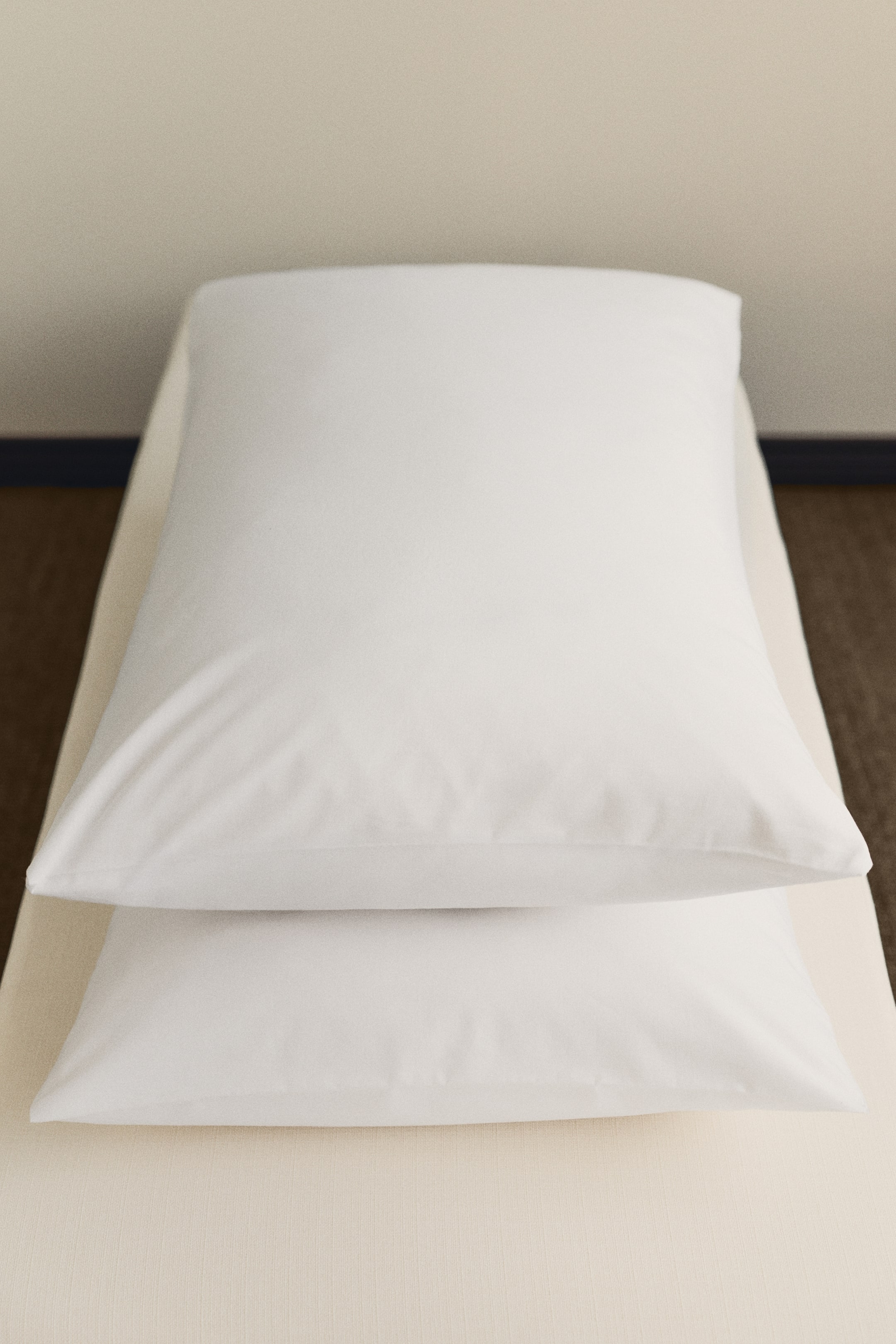 Agrandir l'image: Deux oreillers rectangulaires blancs en tissu lisse sont empilés, l'un reposant sur l'autre, tous deux orientés vers l'avant.