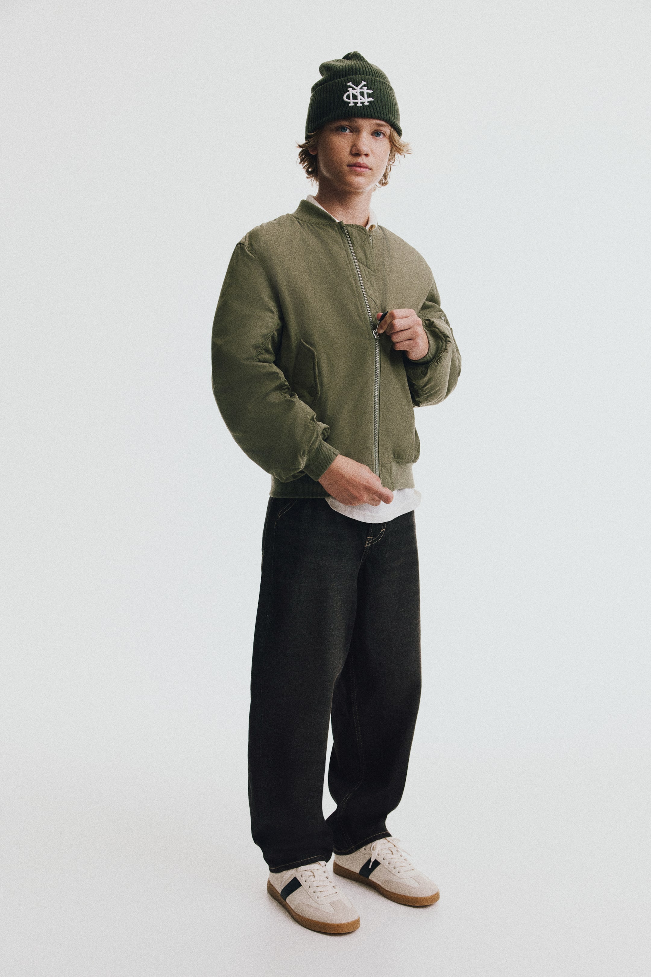 Grotere afbeelding bekijken: Baggy jeans in een vervaagde zwarte denimwassing worden getoond vanuit een driekwart vooraanzicht, waarbij een losse, wijde pijpsilhouet wordt benadrukt. De jeans hebben subtiele contrasterende stiksels en rusten over crèmekleurige sneakers.