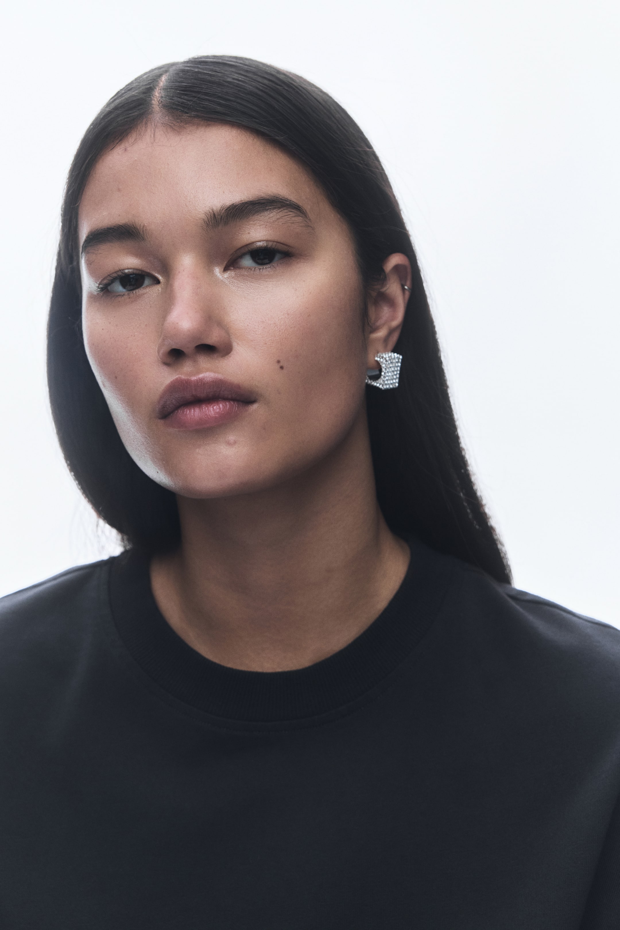 View larger image: A chunky, silver-toned U-shaped earring is being worn on an ear, with its open end facing downwards. Its entire surface is covered in small, sparkling crystals.