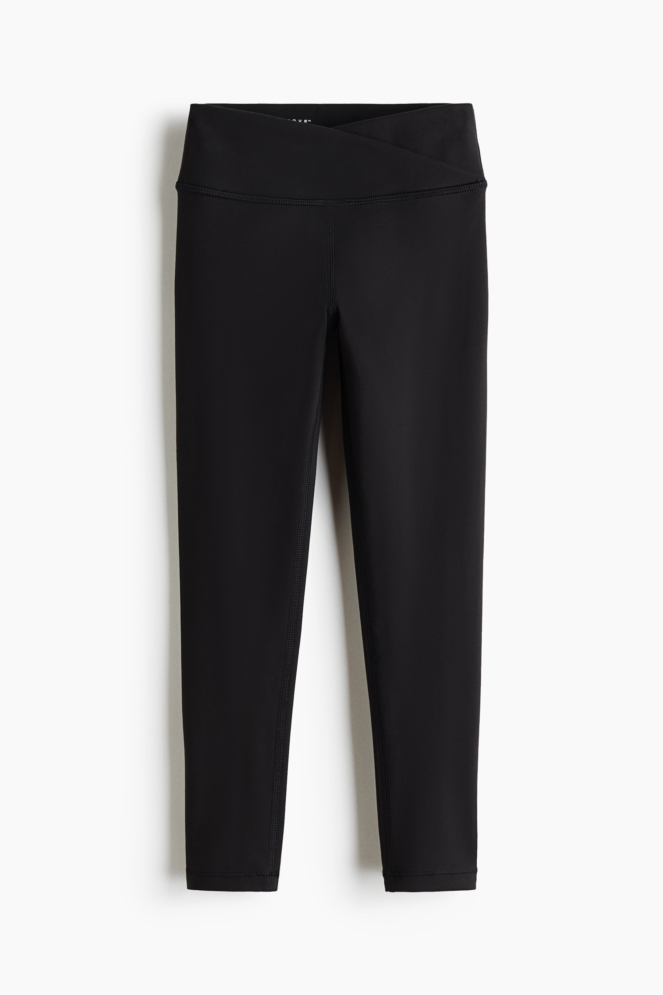 View larger image: Black sports leggings with DryMove™ are lying flat, presenting a front view. They feature a wide, crossover waistband, visible flatlock seams along the legs, and a cropped length.