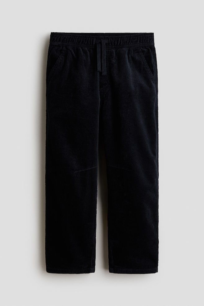 Eine schwarze Cord-Jogginghose ist von vorne zu sehen und Ã¼berzeugt mit strukturiertem Rippenstoff, einem elastischen Bund mit verstellbarem Kordelzug und schrÃ¤gen Seitentaschen. Die Hose ist mit einem Fake-ReiÃverschluss sowie einer legeren Barrel-Leg-Silhouette gestaltet. - 1