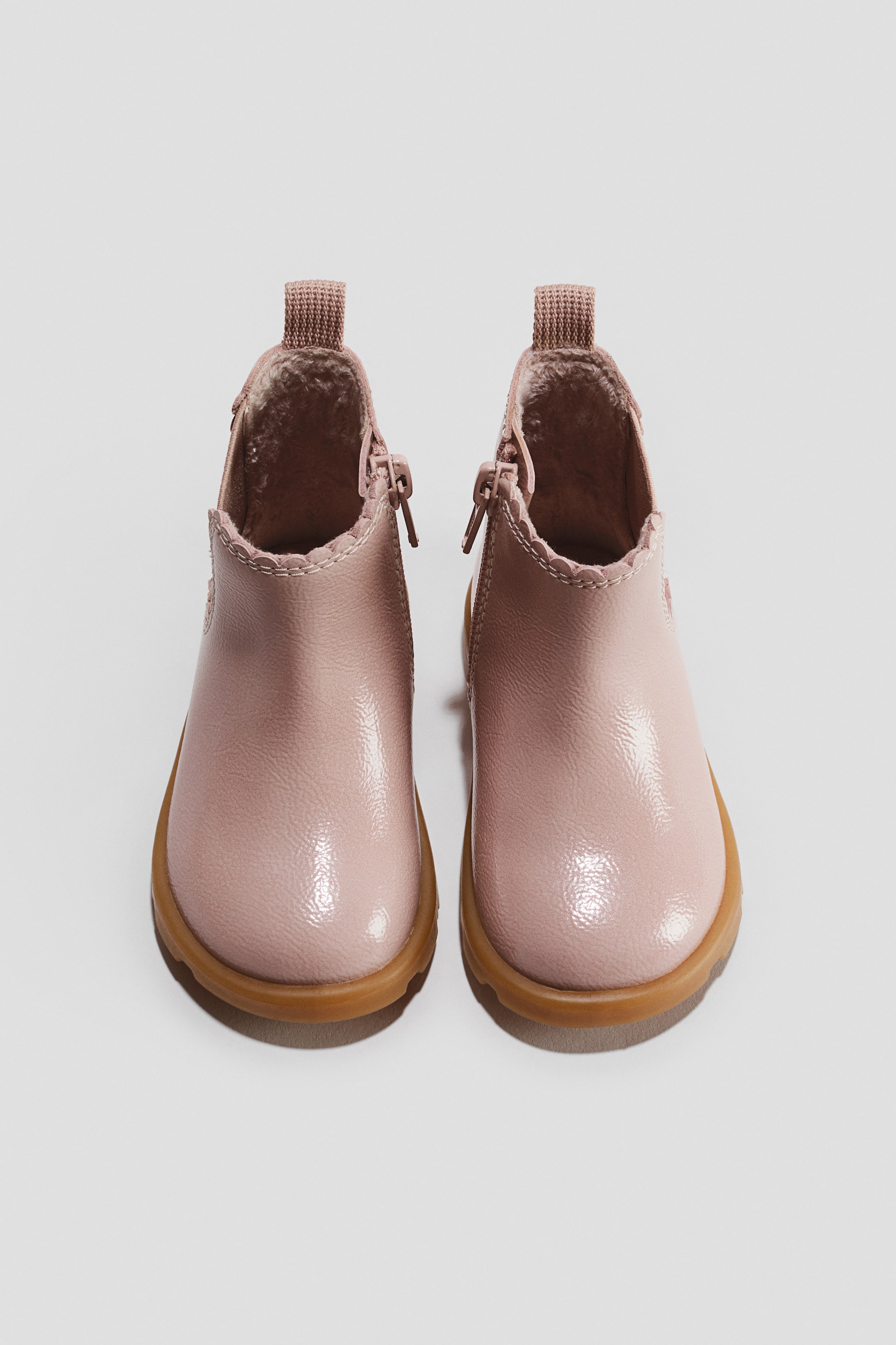 Grösseres Bild ansehen: Ein Paar rosa Chelsea-Stiefeletten ist von vorne ausgerichtet und präsentiert ein glänzendes Finish, runde Zehen und hellbraune Gummiaußensohlen. Die Stiefeletten verfügen über seitliche Reißverschlüsse innen, gewellte Details am Schaftabschluss, Zuglaschen hinten und ein weiches Innenfutter.
