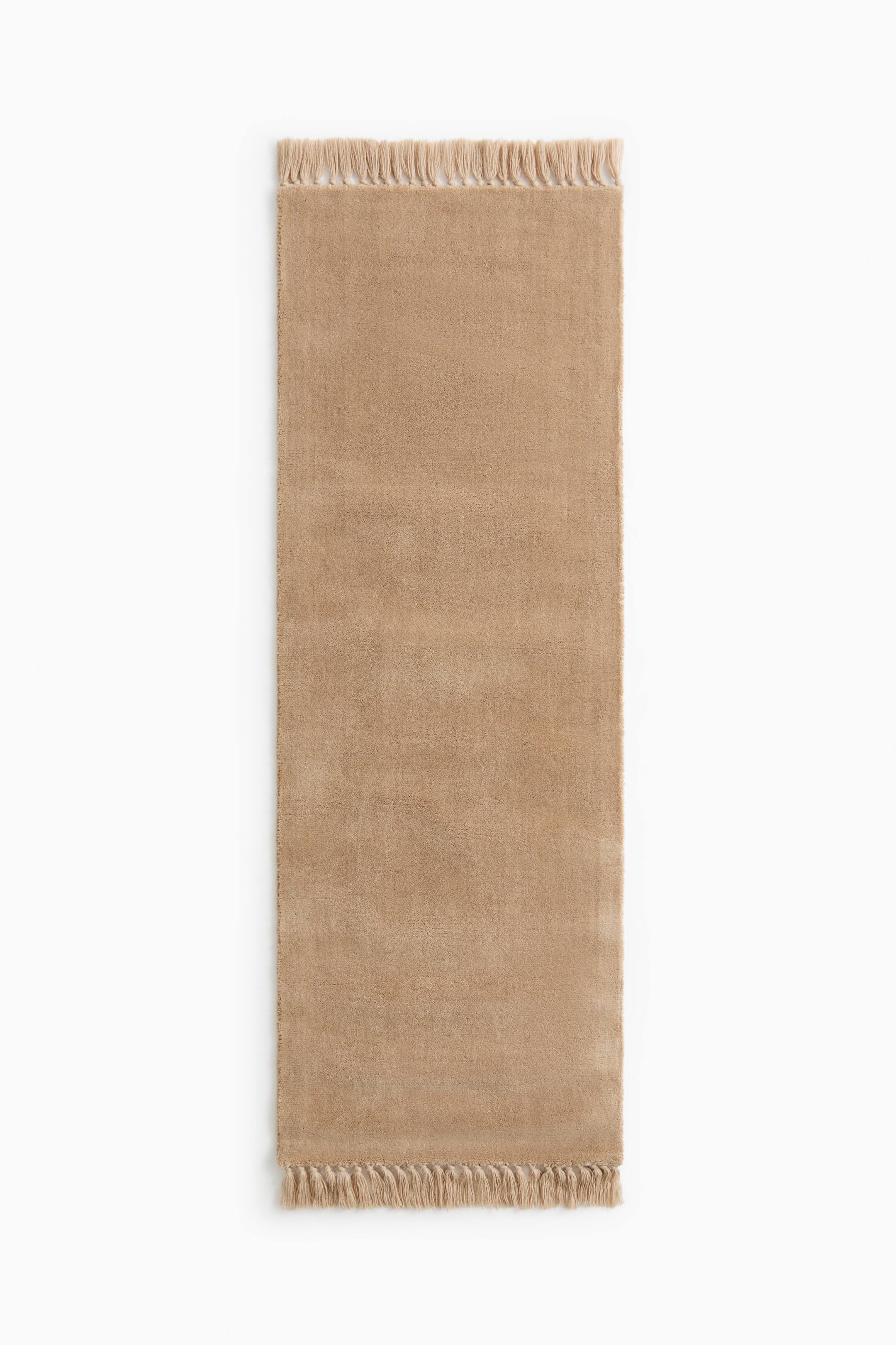 Visa större bild: En rektangulär beige gångmatta visas i frontvy, med en mjuk, fluffig struktur och en enhetlig färg. Mattan har matchande beige fransar längs båda de kortare ändarna.