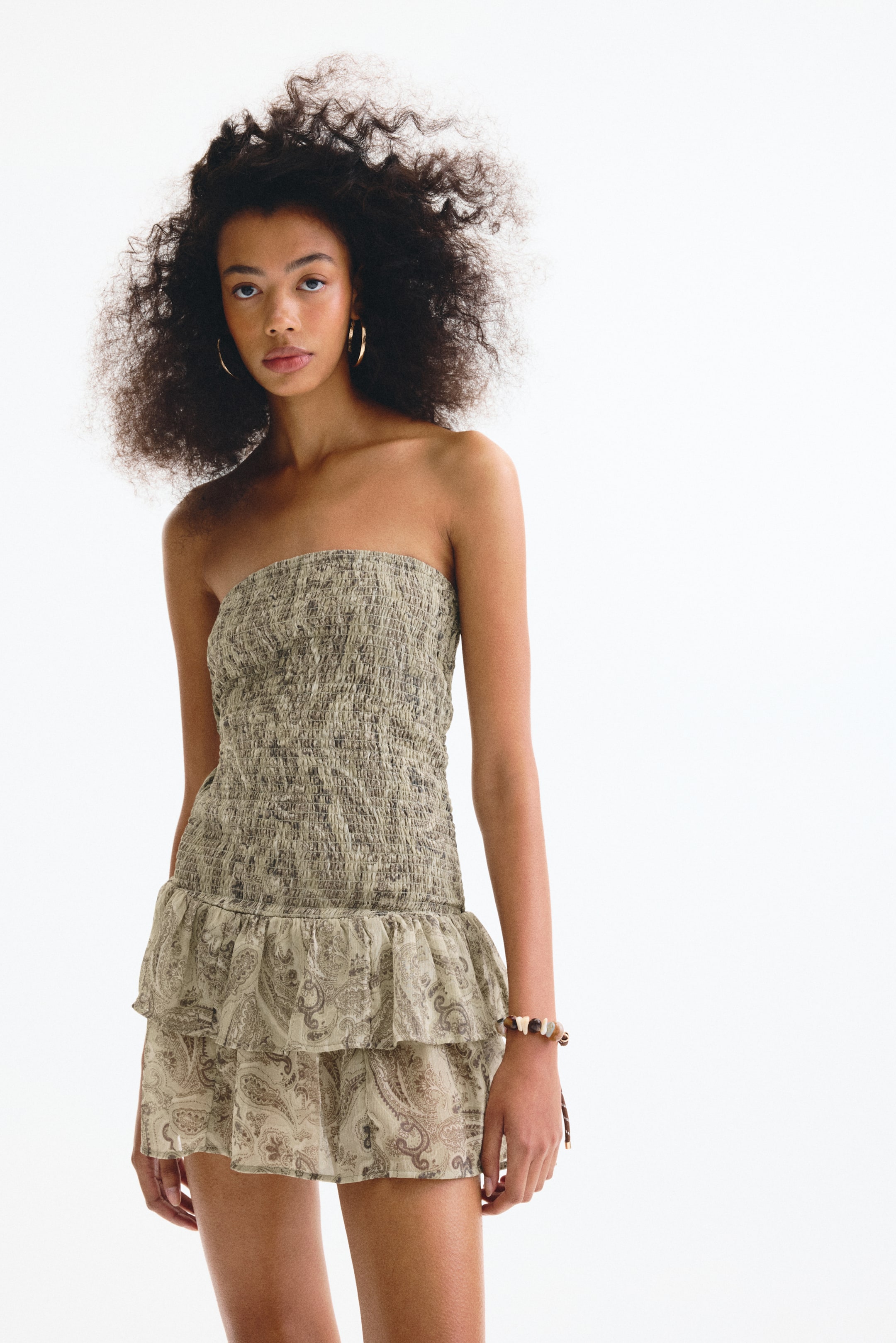 View larger image: A strapless mini dress showcasing a shirred bodice in a textured khaki, flowing into a two-tiered ruffled skirt adorned with a beige paisley print, displayed front-facing.