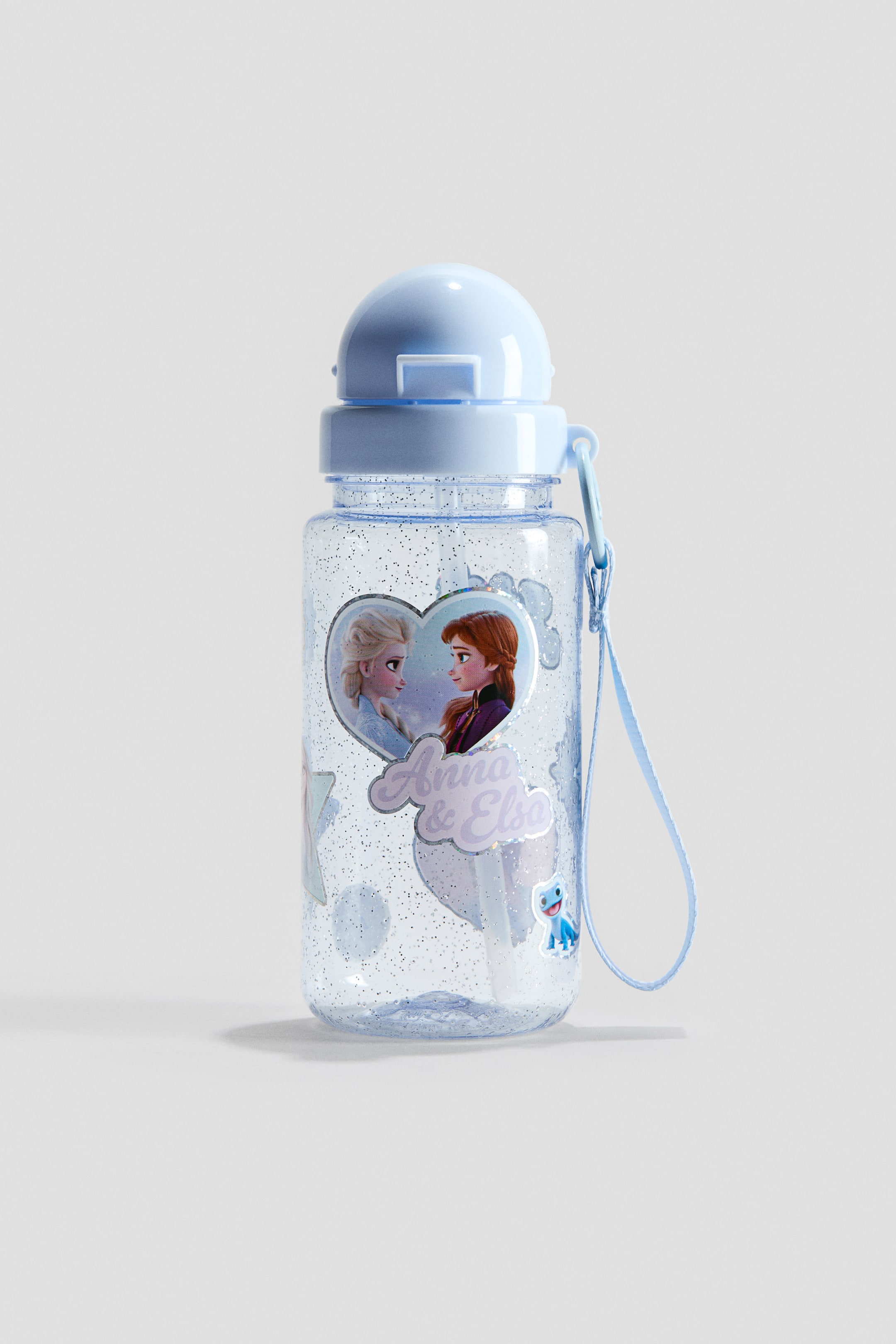 View larger image: A plastic water bottle stands front-facing, showcasing a clear, glitter-infused body with a print motif of Anna and Elsa in a heart shape and other small character graphics. It is topped with a light blue non-drip lid, which incorporates a straw, and features a detachable light blue fabric wrist strap.