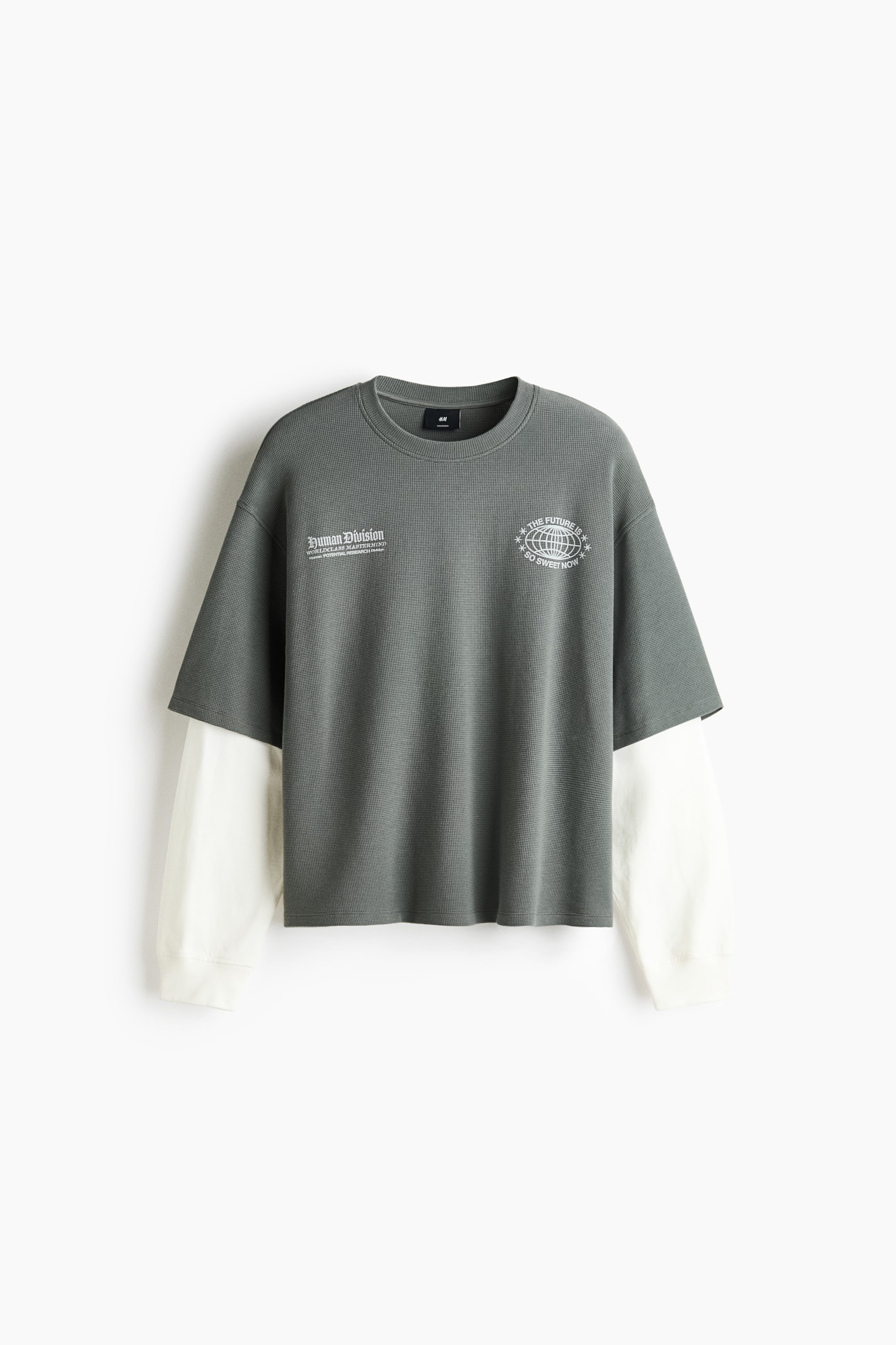 Grösseres Bild ansehen: Ein mehrlagiges Langarm-T-Shirt ist von vorne zu sehen und präsentiert eine dunkelgraue, strukturierte äußere Schicht mit kurzen Ärmeln sowie kontrastierende, cremefarbene lange Ärmel, die darunter hervorschauen. Die äußere Schicht zeigt zwei weisse Grafikdrucke auf der Brust und verfügt über einen gerippten Rundhalsausschnitt, während die cremefarbenen Ärmel mit gerippten Bündchen abschliessen.
