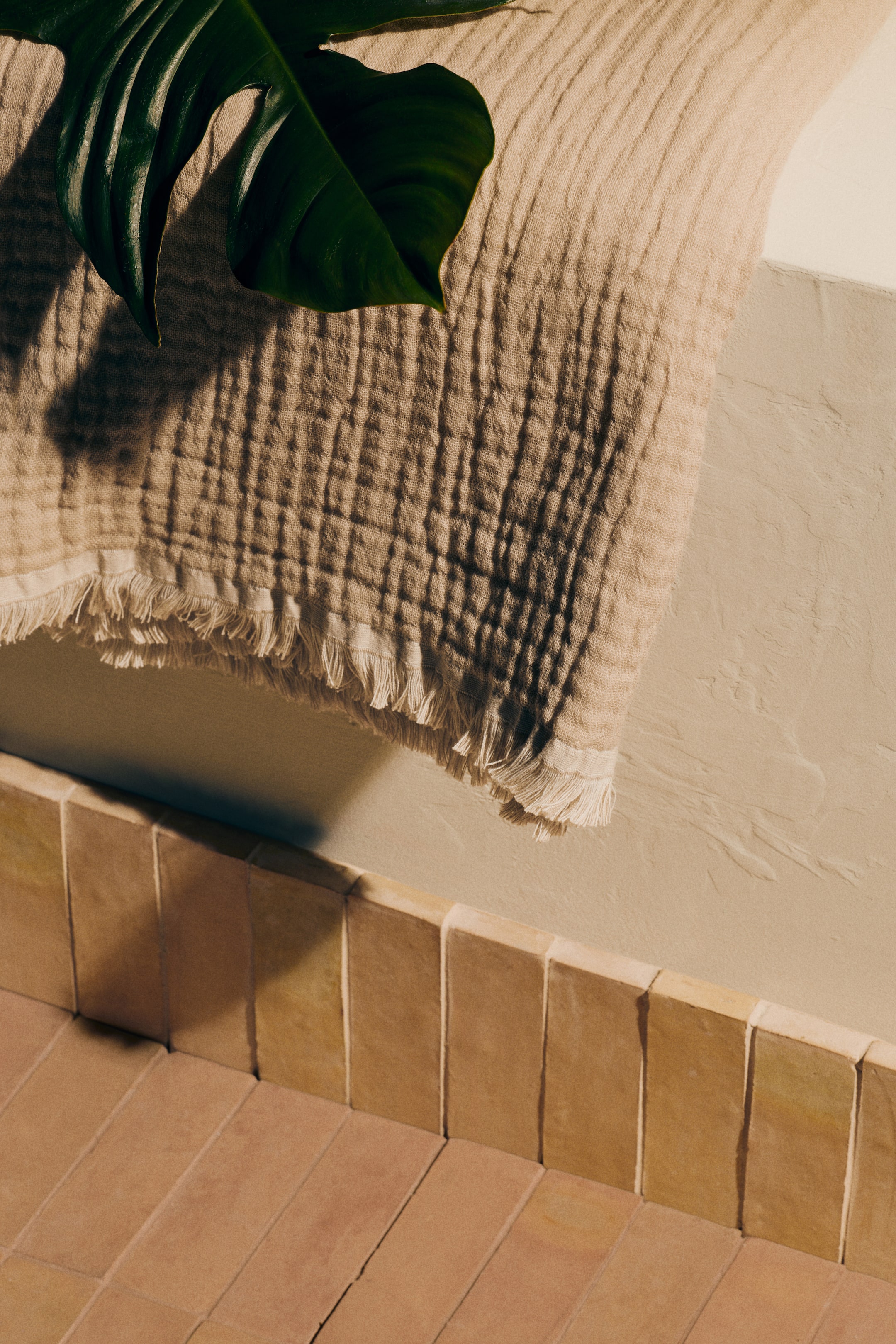 View larger image: A beige double-gauze textile is elegantly draped, showcasing its naturally crinkled texture and a fringed hem. A large green leaf rests gracefully on its surface.