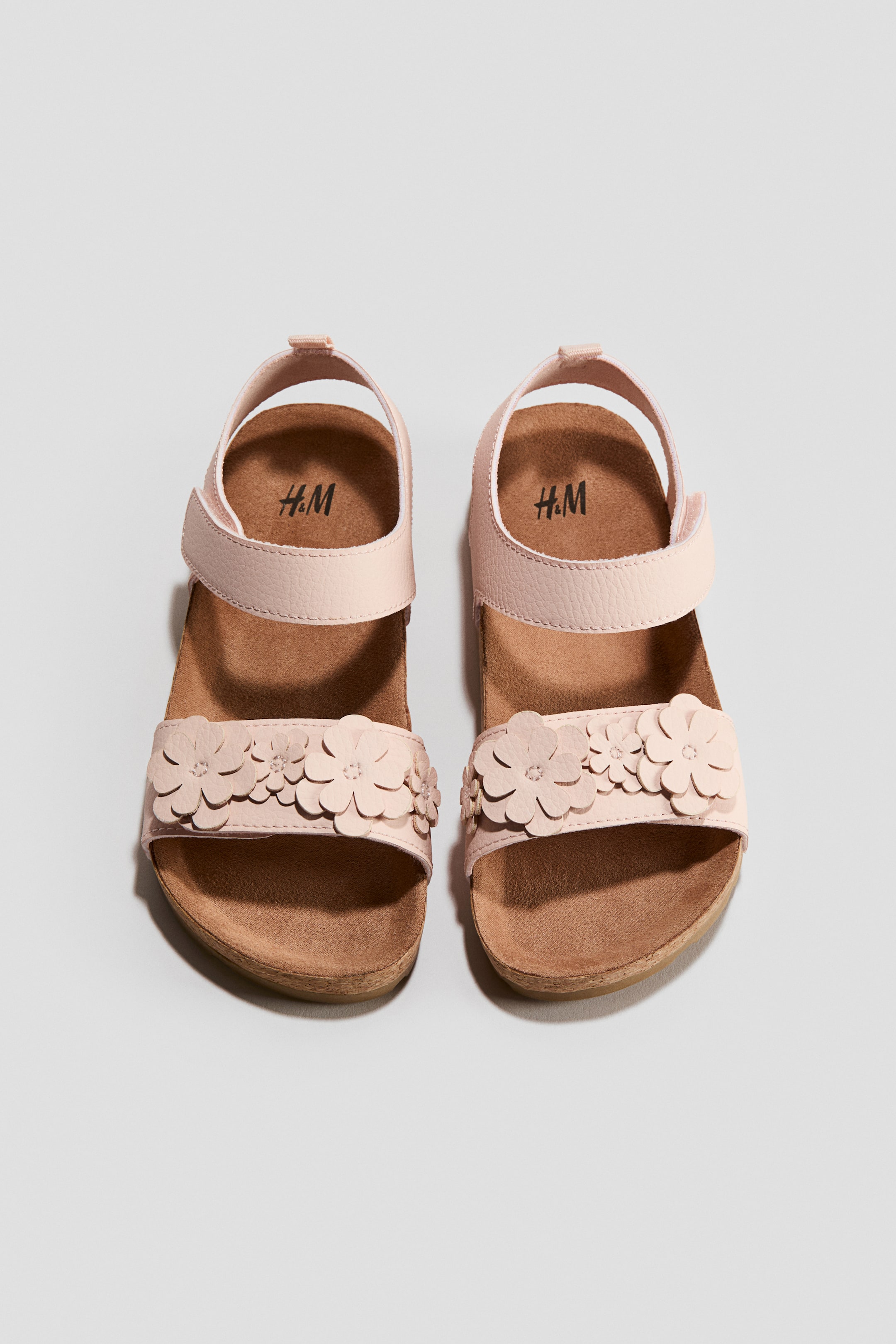 View larger image: Shown from the front, a pair of light pink sandals features a foot strap decorated with multiple 3D flower appliqués and an ankle strap with an adjustable hook-and-loop fastening. The sandals showcase molded insoles and fluted soles.