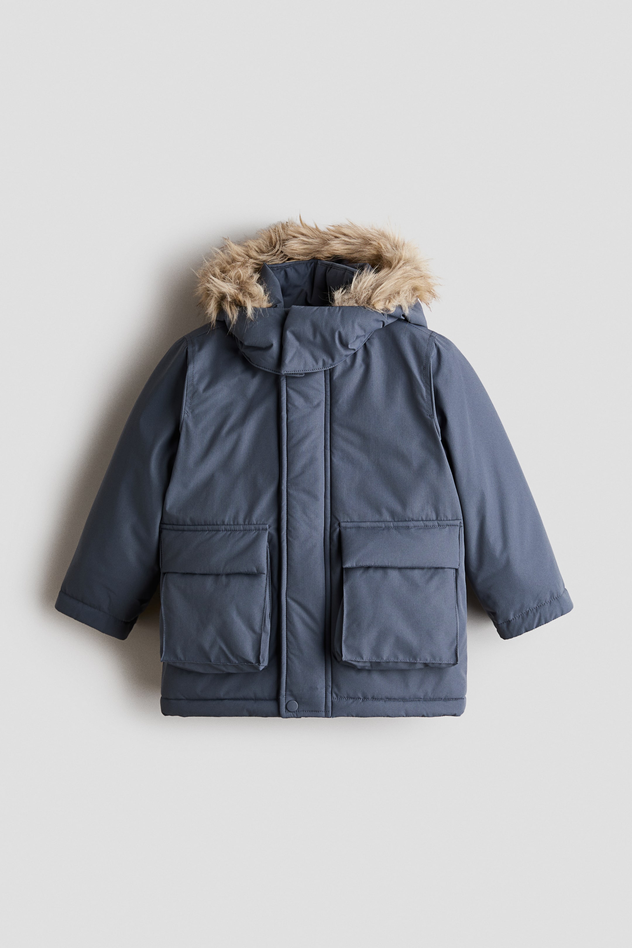 Ver imagen más grande: Una parka infantil de invierno en azul pizarra está de frente, con capucha ribeteada con pelo sintético marrón claro, cierre delantero oculto y dos grandes bolsillos de parche inferiores con solapas.