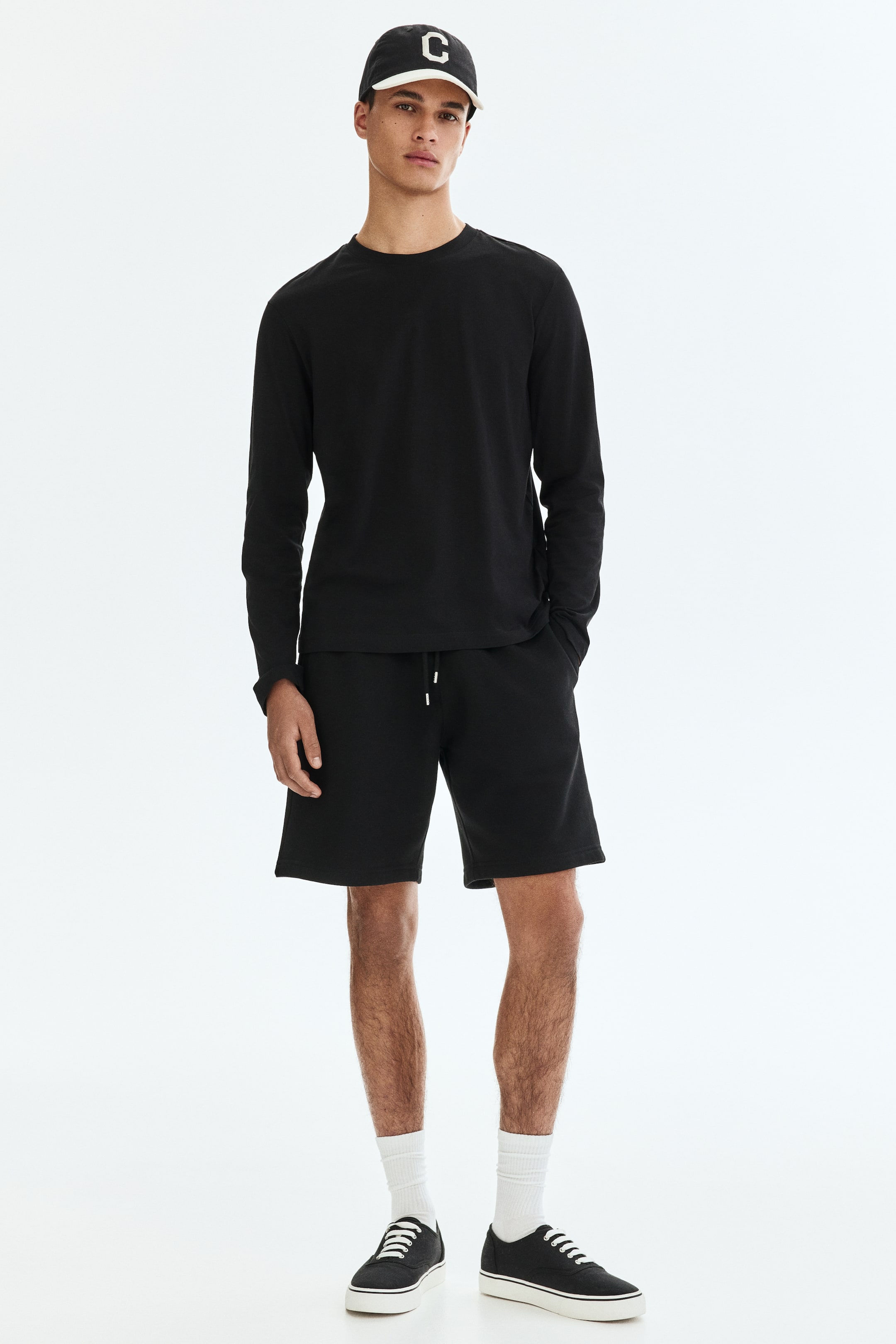 Zobacz większy obraz: Modelka nosi czarne szorty z dzianiny. Szorty mają widoczny sznurek w pasie oraz kieszenie po bokach, a ręka modelki spoczywa w jednej z kieszeni.