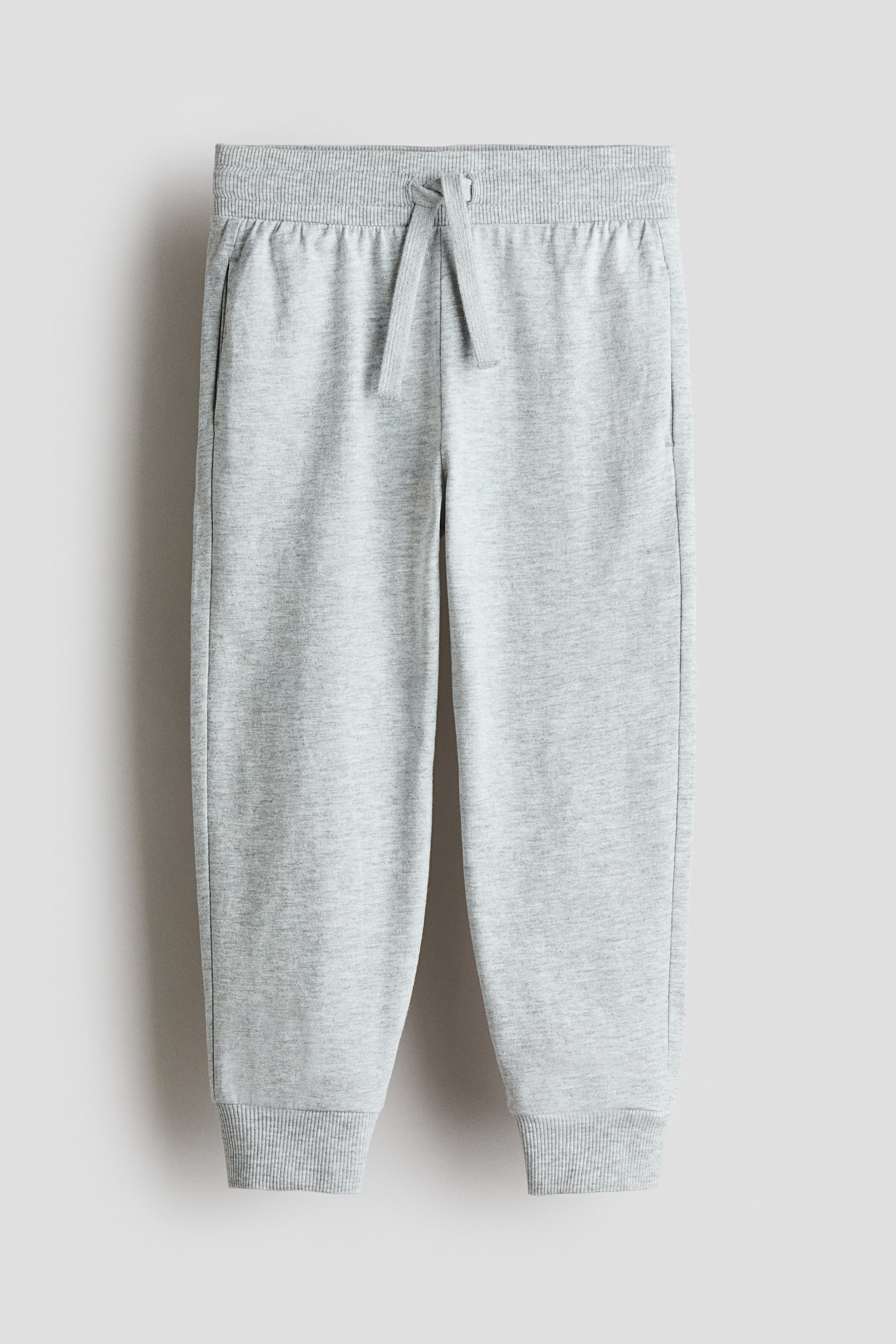 View larger image: Heather grey sweatpants feature a ribbed waistband with a drawstring tied at the front. They also have two side pockets and ribbed cuffs at the ankles.