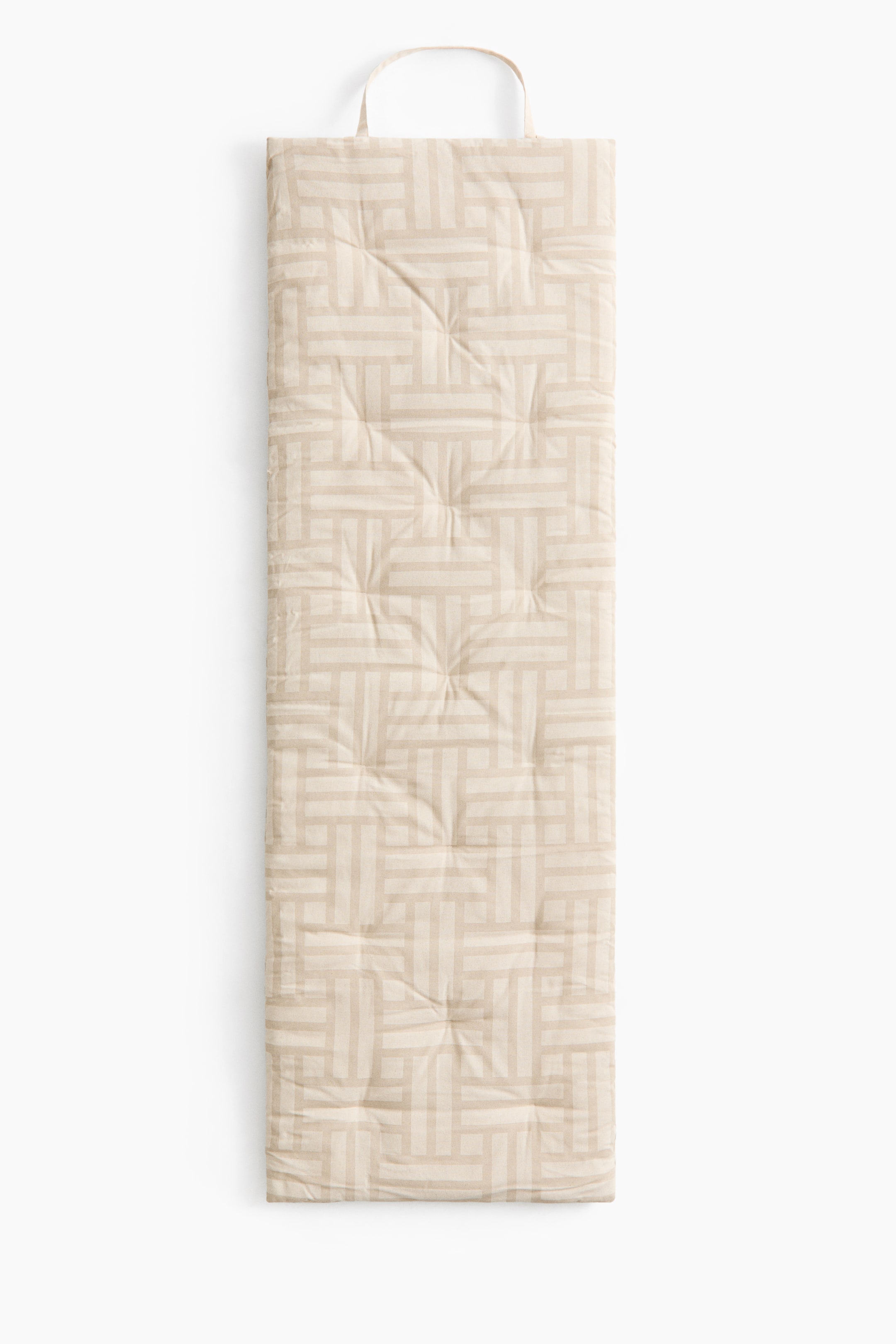 Se større billede: En polstret strandmadras ligger fladt og viser et beige stof med et geometrisk mønster af sammenflettede rektangler. Den har tuftede detaljer over hele overfladen og et stofhåndtag i den ene ende.