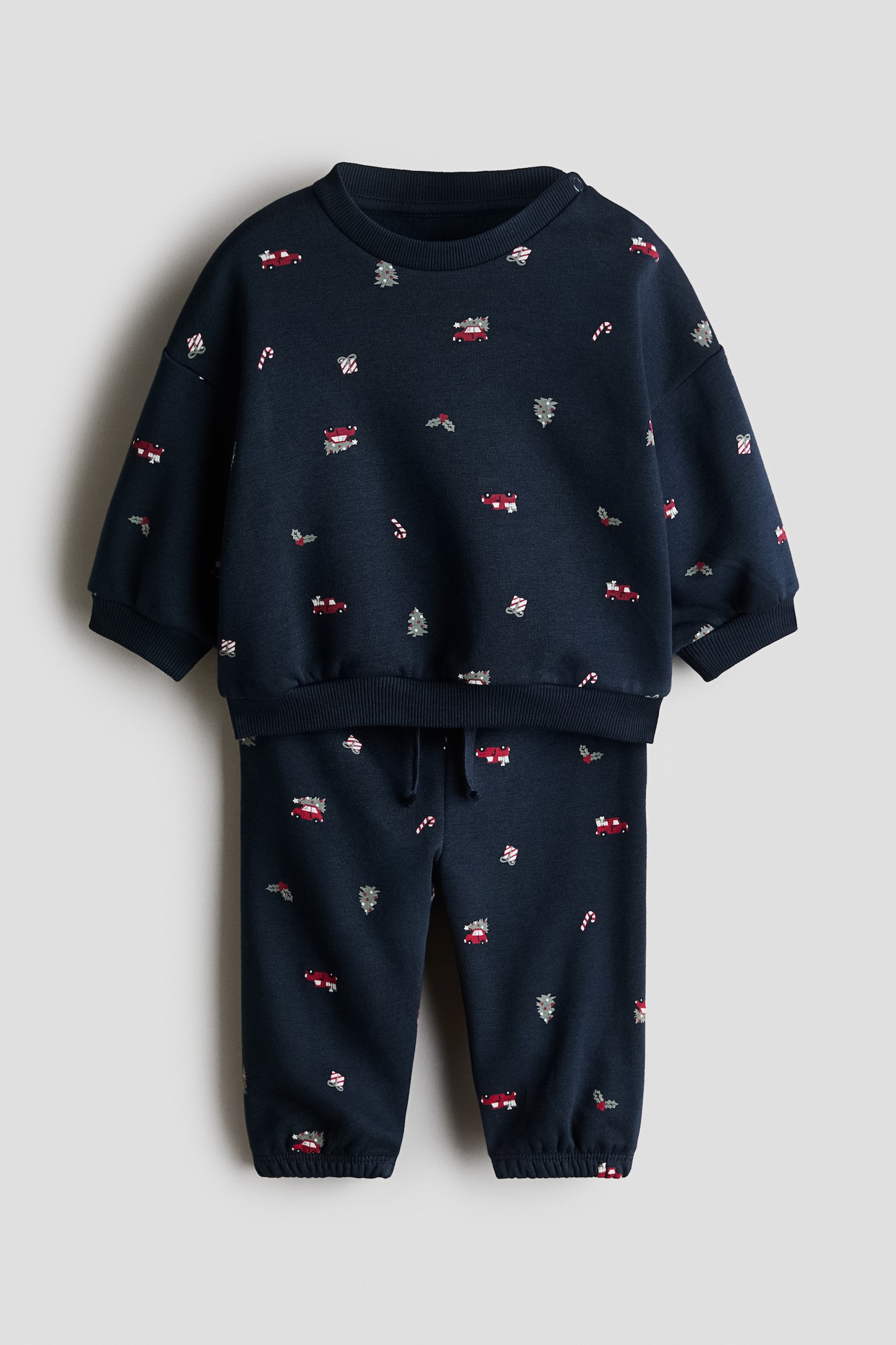 Ein zweiteiliger Sweat-Set in Marineblau mit Frontansicht zeigt einen allover weihnachtlichen Print aus kleinen roten Autos, Zuckerstangen und ChristbÃ¤umen. Das Set besteht aus einem Langarm-Sweatshirt mit geripptem Rundhalsausschnitt, Ã¼berschnittenen Schultern und gerippten AbschlÃ¼ssen sowie einer passenden Sweatpants mit Kordelzugbund und elastischen BeinabschlÃ¼ssen.