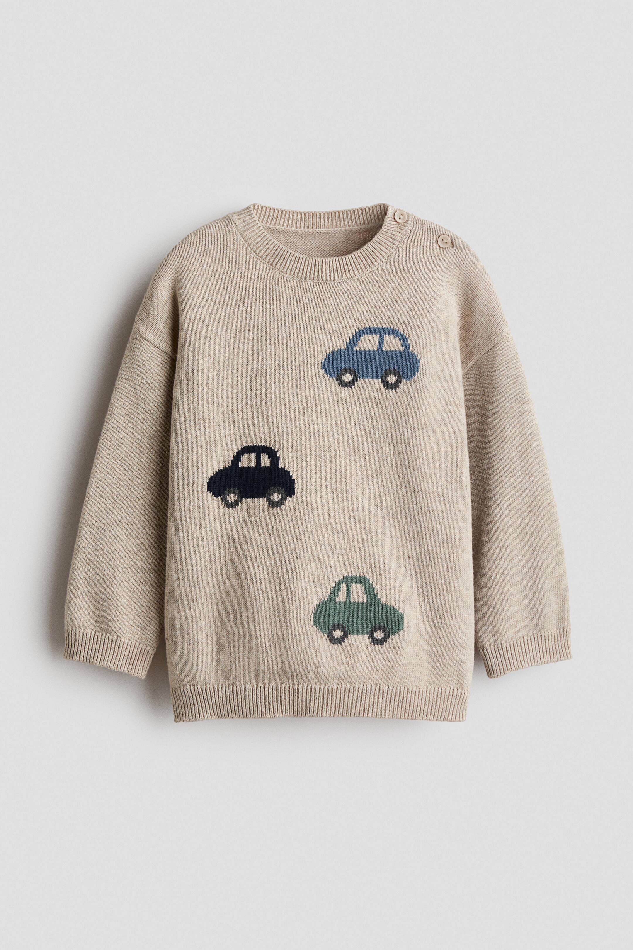View larger image: A beige knit sweater is laid flat, featuring three knitted car motifs in blue, dark blue, and green. It has a ribbed crew neck, long sleeves with ribbed cuffs, a ribbed hem, and two small, round buttons on the left shoulder.