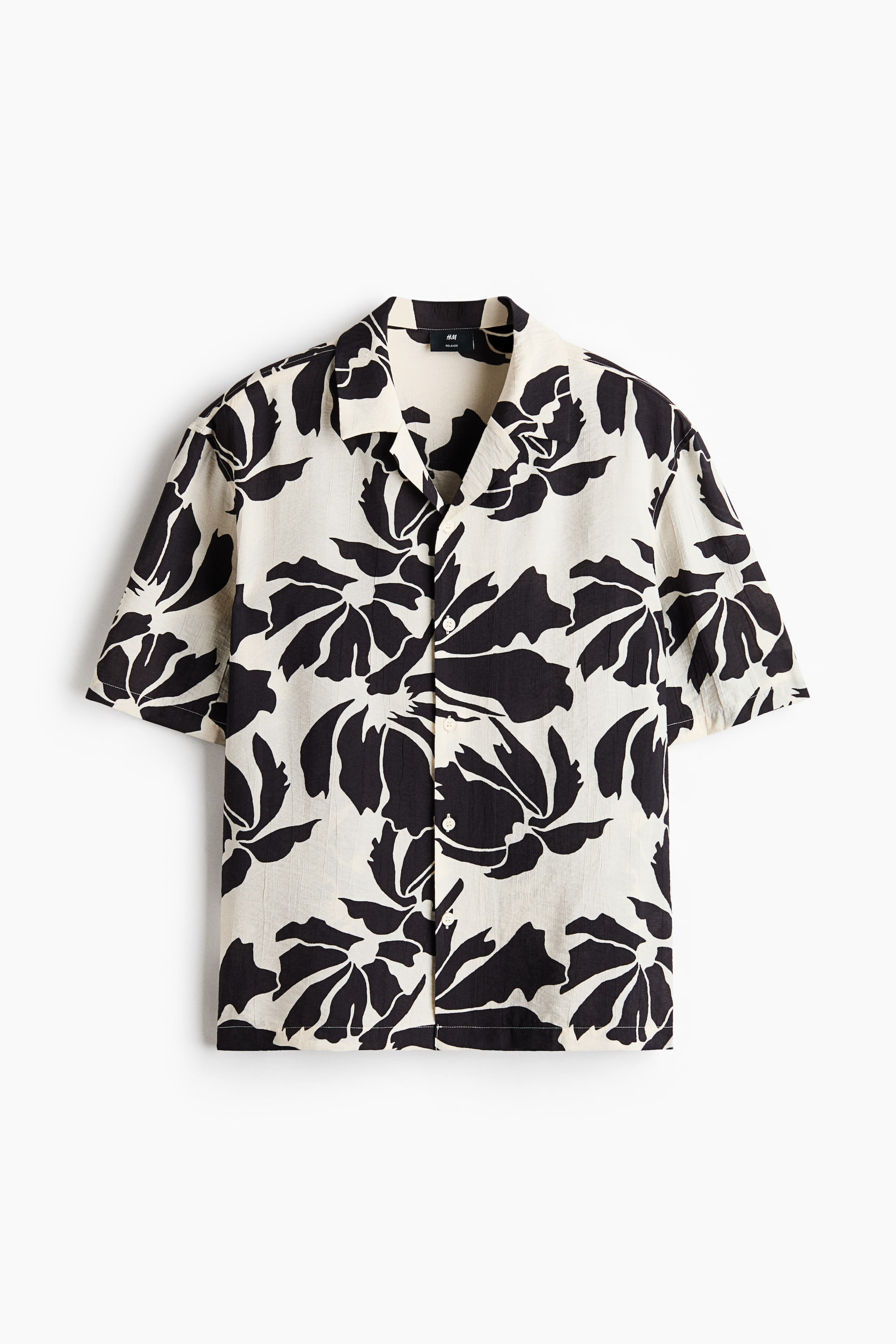 View larger image: A short-sleeved shirt showcasing a black abstract floral pattern on an off-white textured fabric. It is crafted with a revere collar and a front button placket adorned with white buttons.