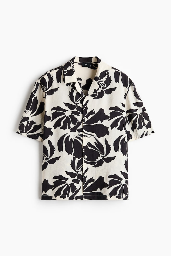 A short-sleeved shirt showcasing a black abstract floral pattern on an off-white textured fabric. It is crafted with a revere collar and a front button placket adorned with white buttons. - 1