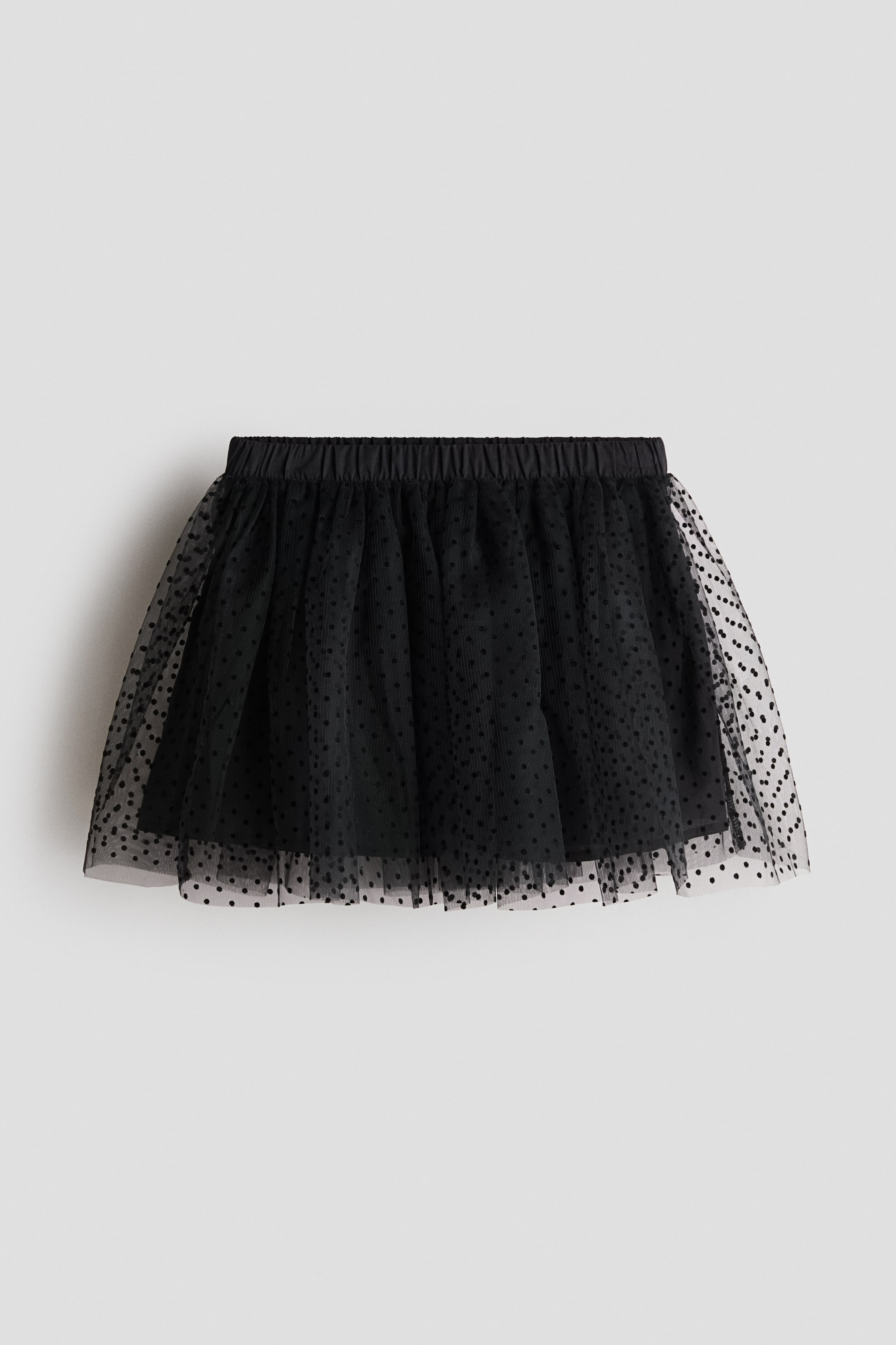 View larger image: A black tulle skirt featuring an elasticated, gathered waistband and a sheer outer layer with small black polka dots, layered over a solid black lining.