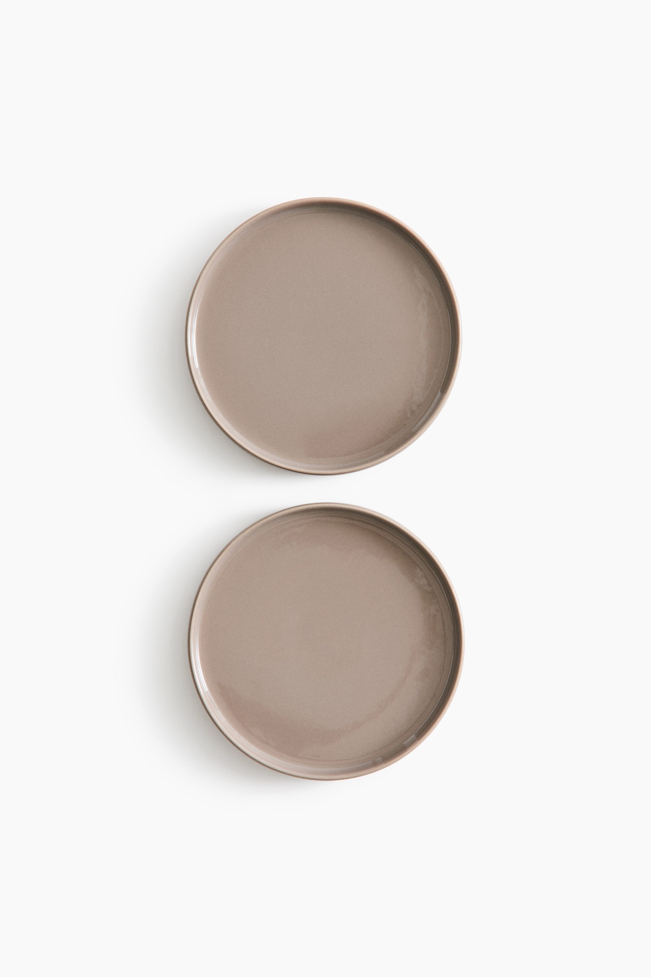 Visa större bild: Två runda stengodsassietter i mellanstorlek med blank taupe-finish står vertikalt sedda uppifrån. Båda assietterna har en slät, reflekterande yta och en lätt upphöjd kant.