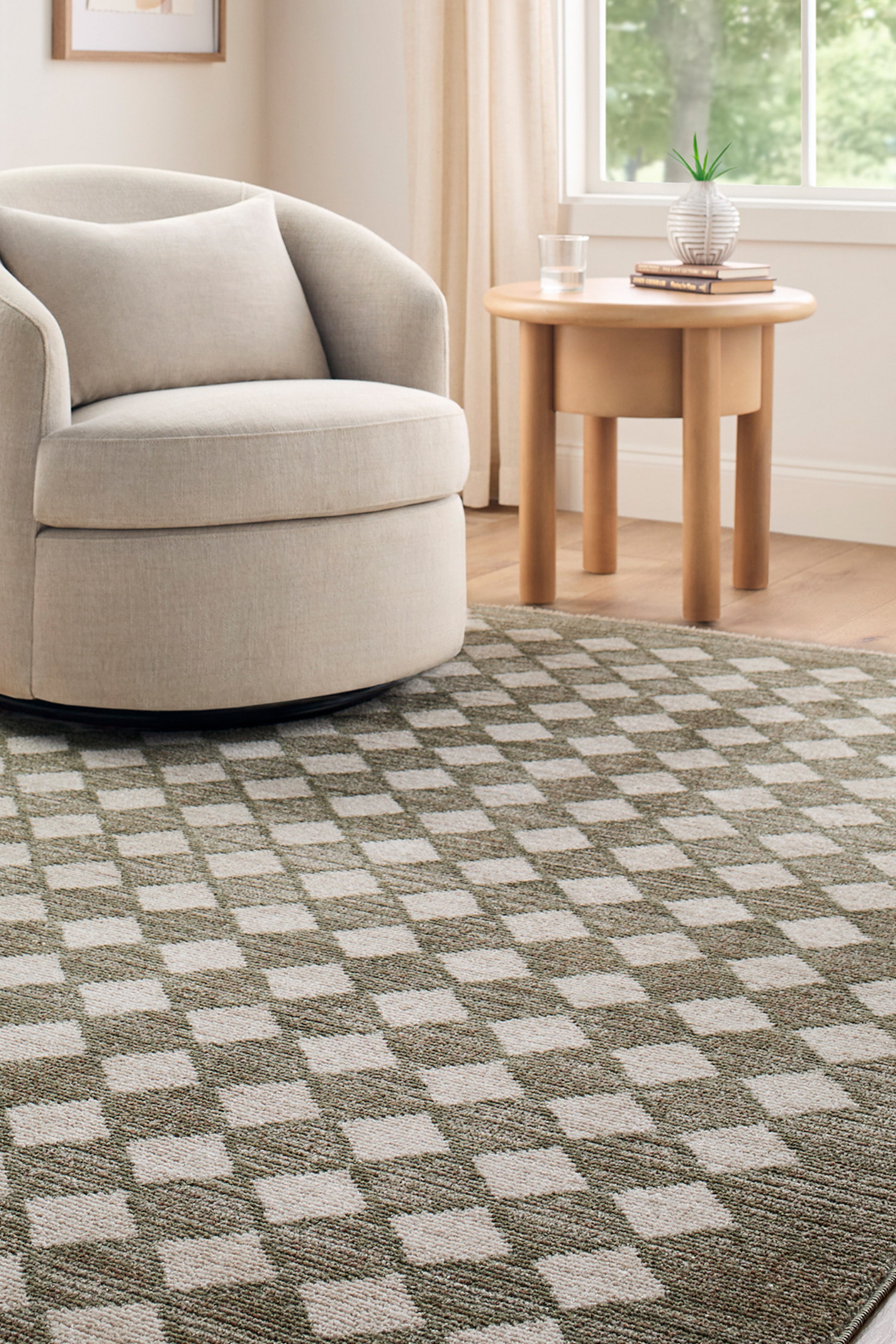 View larger image: A rectangular rug featuring a chequerboard pattern of alternating deep olive green and off-white squares. The rug displays a visible woven texture and extends from the foreground towards the background, partially visible under a chair and a side table.