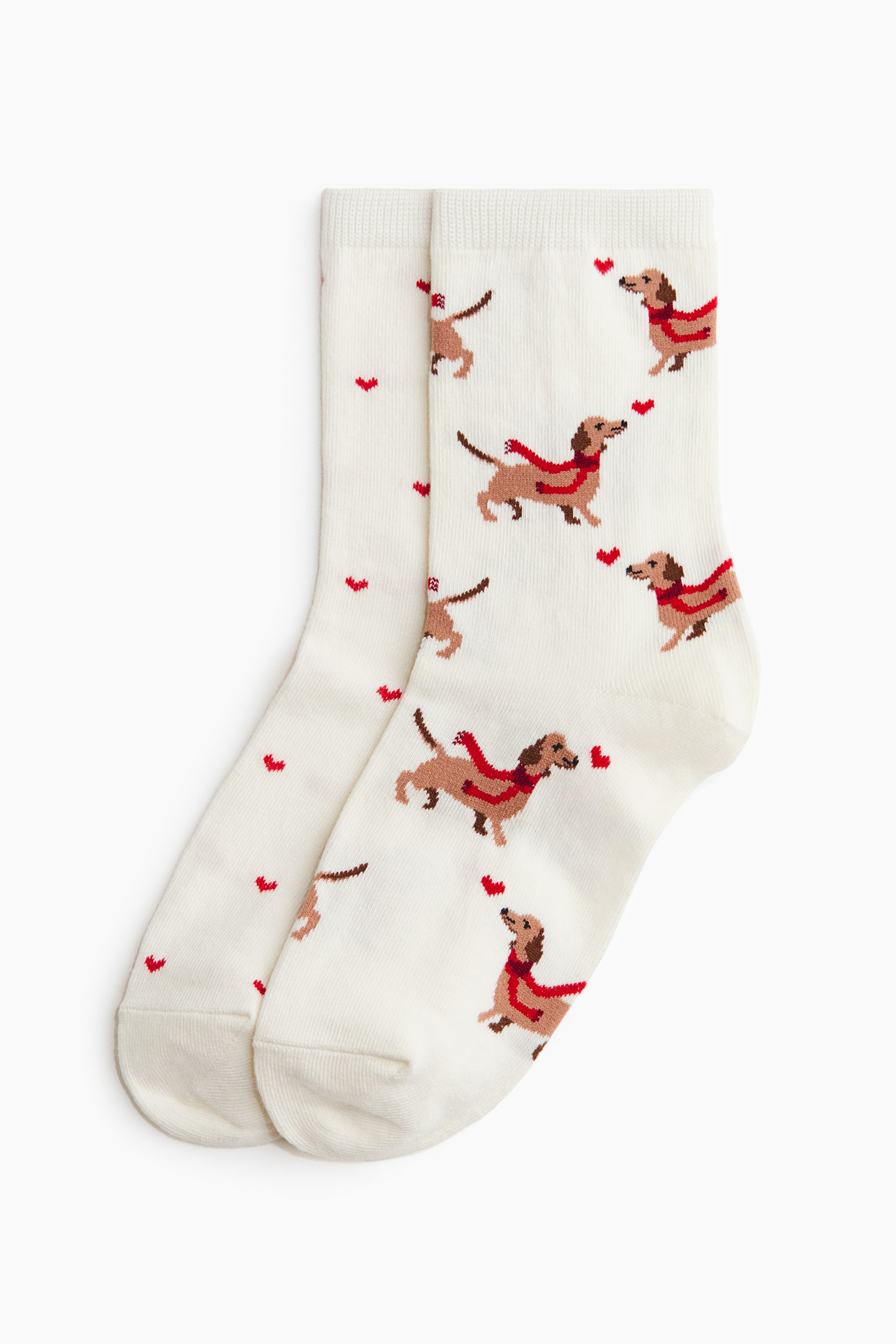 View larger image: A pair of fine-knit socks features a cream background with a repeating pattern of brown dachshunds wearing red scarves and small, scattered red hearts. The socks are finished with ribbed cuffs at the top.