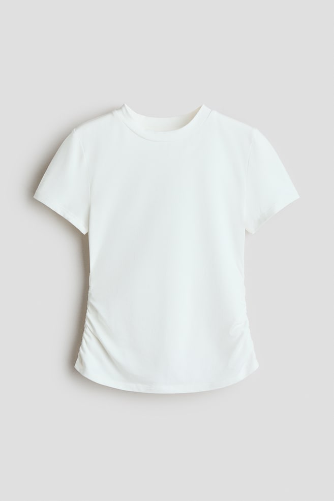 A white short-sleeved t-shirt is facing front, showcasing a crew neckline and a fitted silhouette. Ruched detailing is gathering the fabric along both lower side seams, creating a slightly draped effect across the hem. - 1